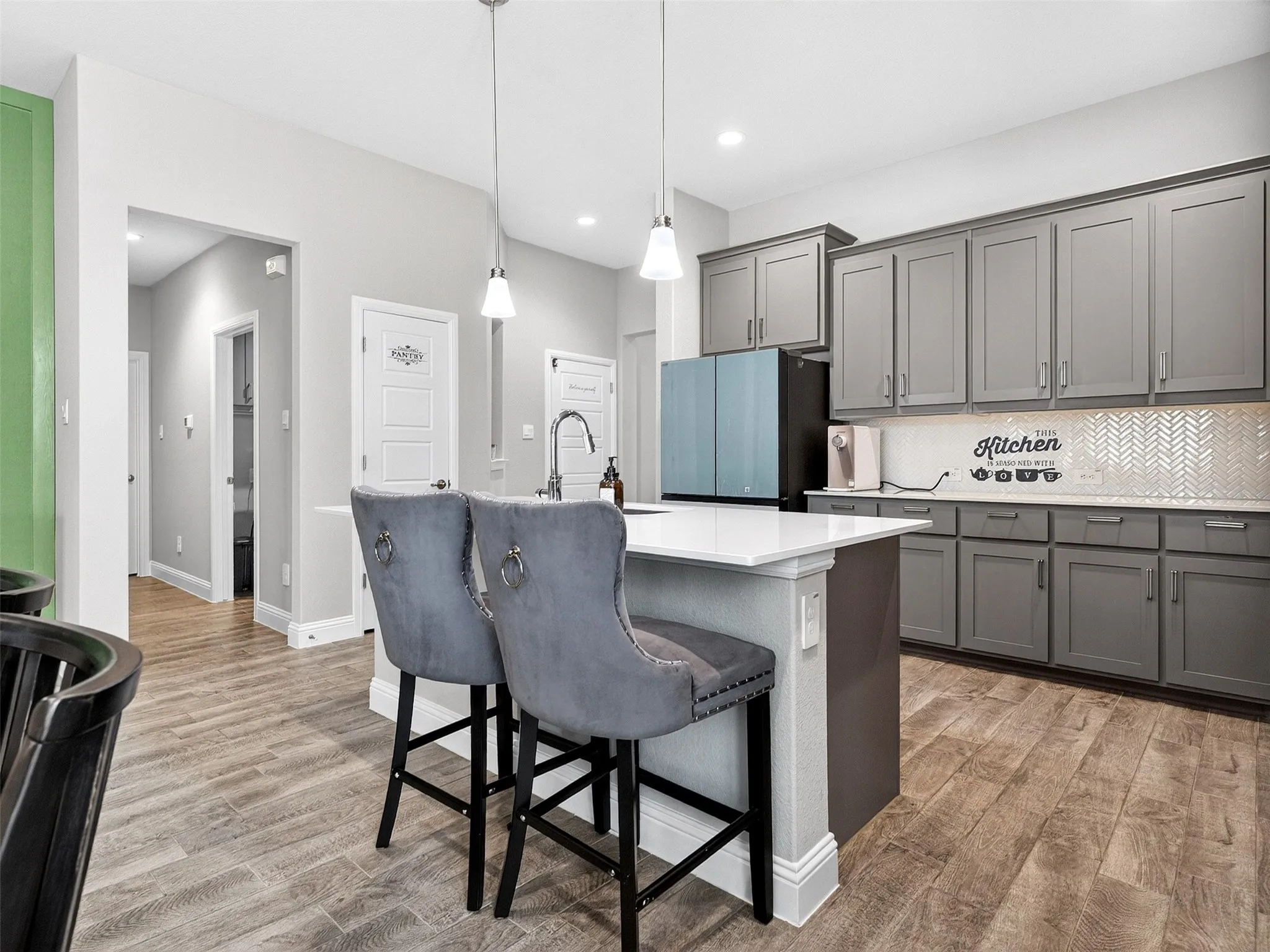 Kitchen featuring an island with a white countertop, gray cabinetry, wood-finish flooring, and a white herringbone tile backsplash