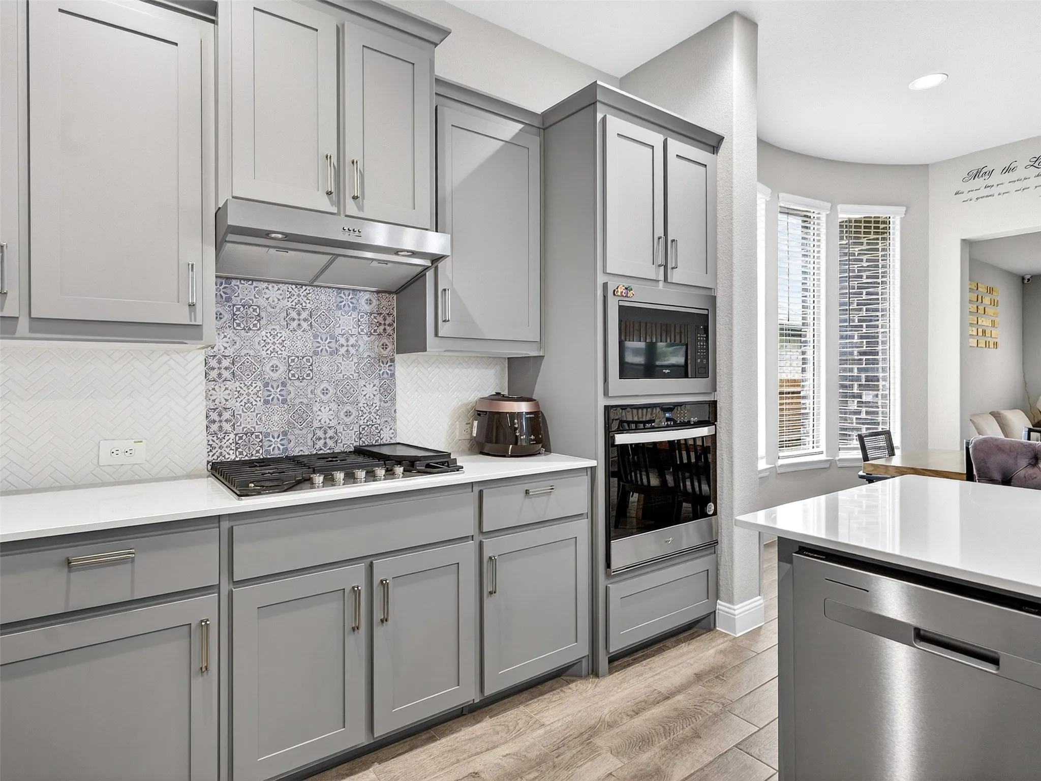 Gray shaker-style cabinetry with stainless steel hardware, white countertops, built-in microwave, integrated wall oven, and a gas cooktop with a decorative tile backsplash