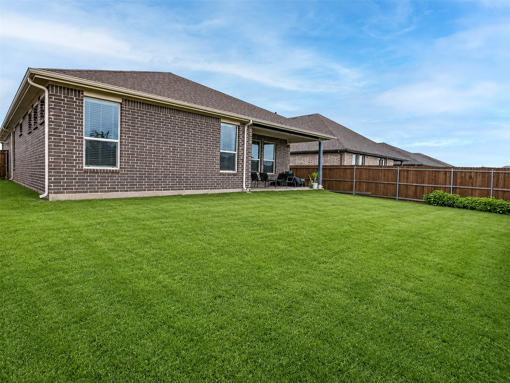 Expansive backyard featuring a manicured lawn, brick exterior, covered patio, and privacy fencing