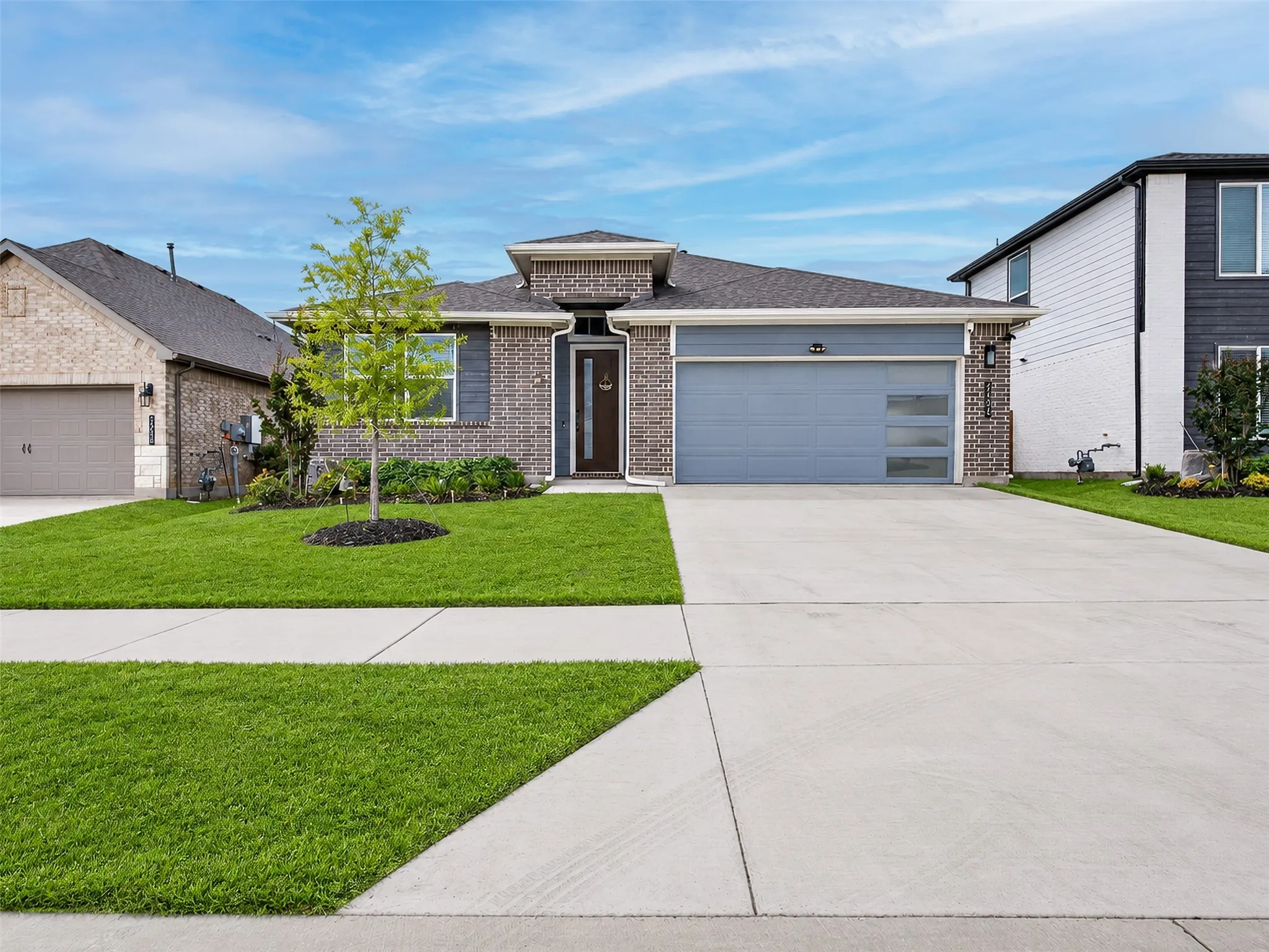 Contemporary brick and siding exterior with a dark-tone entry door, an integrated two-car garage with frosted glass panels, and a well-maintained lawn