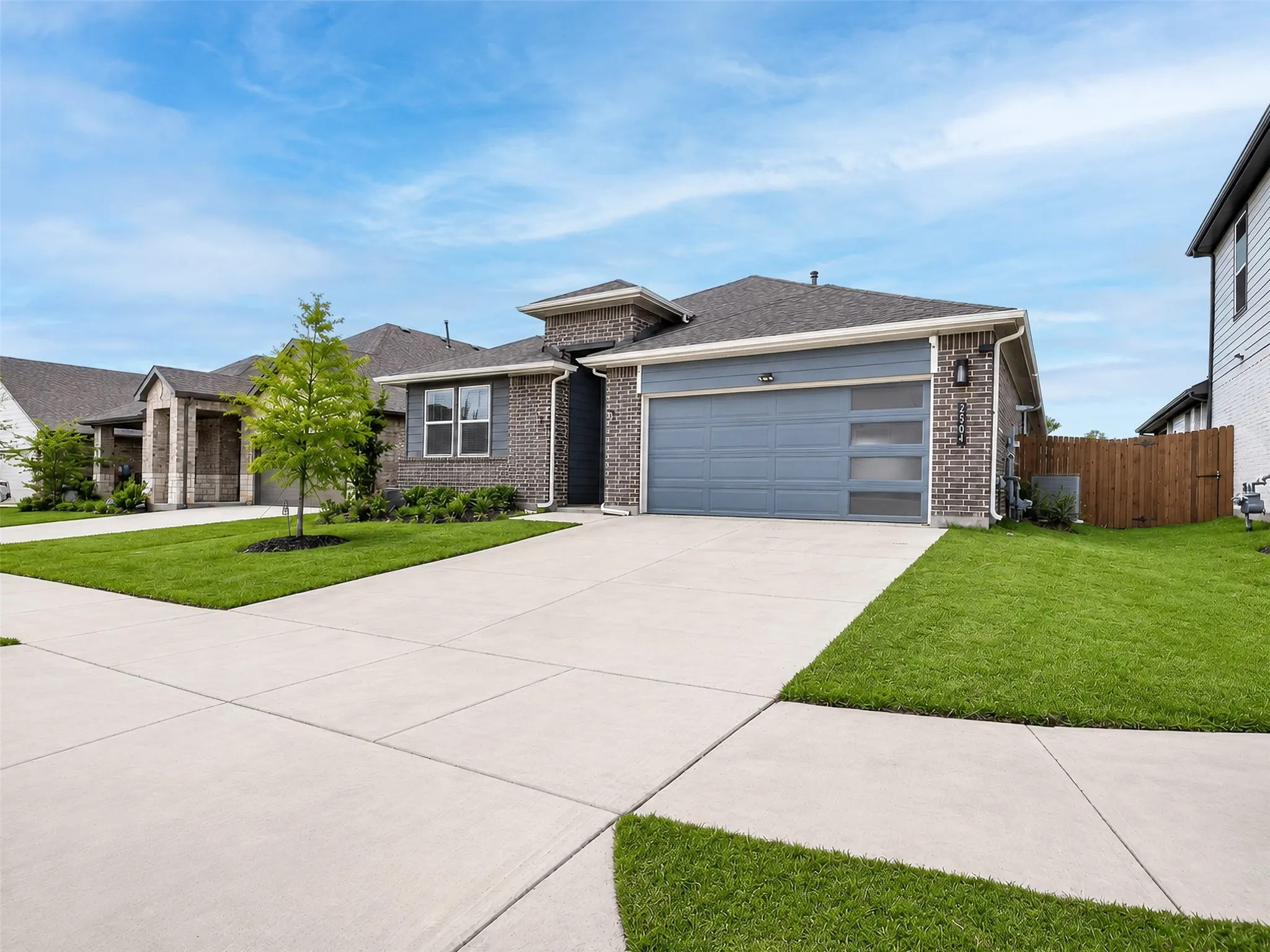 Brick exterior with gray siding accents, attached two-car garage with frosted panel inserts, concrete driveway, and established front landscaping