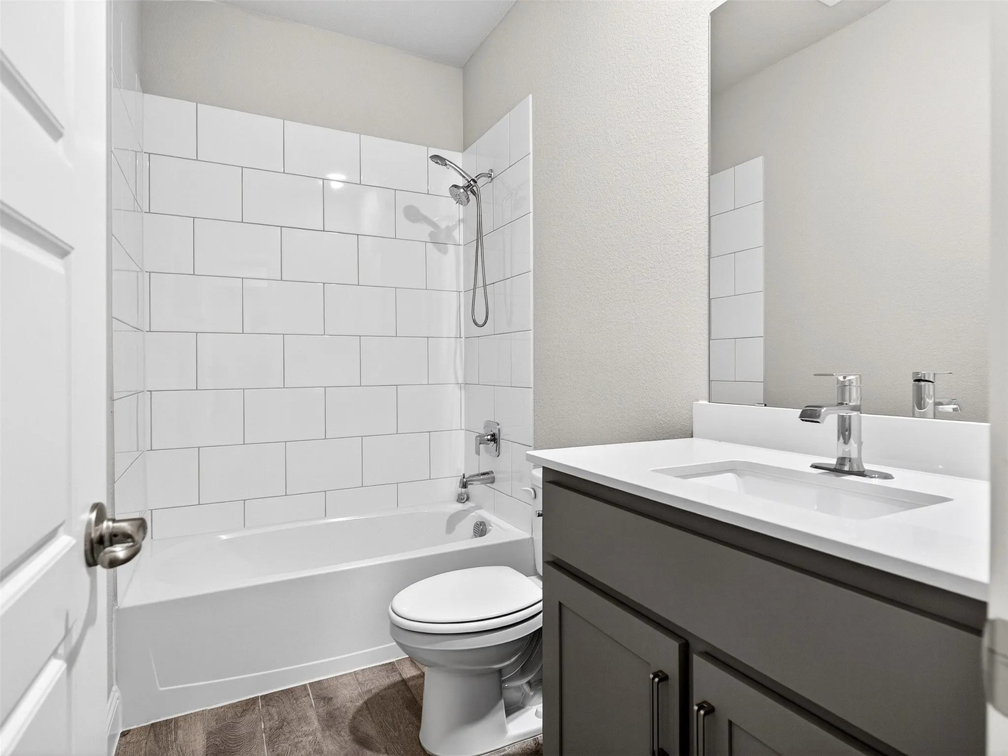 Tub/shower combination with white subway tile surround, single vanity with a white countertop, and wood-finish flooring