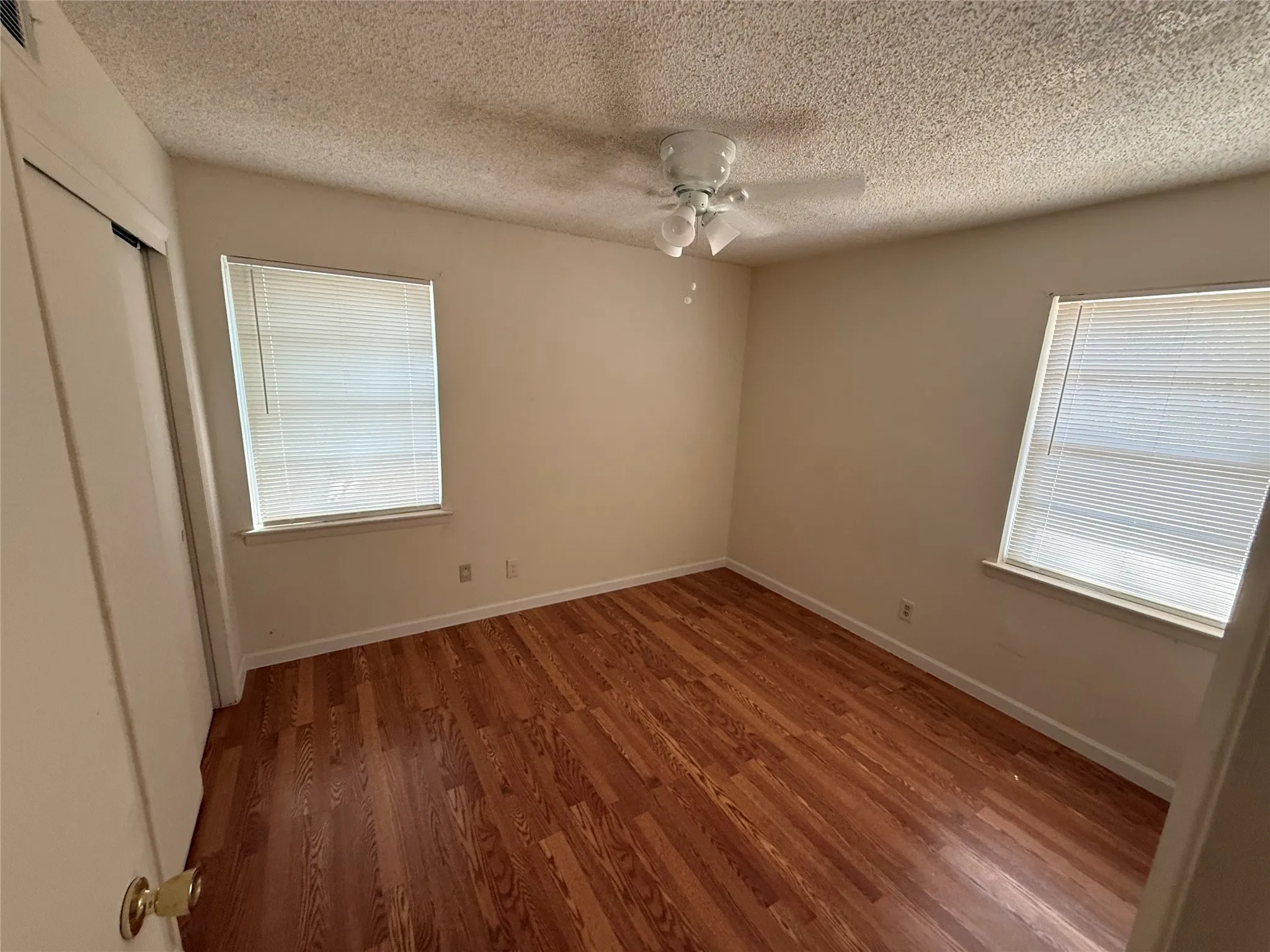 Wood-finish flooring, dual windows with blinds, ceiling fan, and a closet with sliding doors