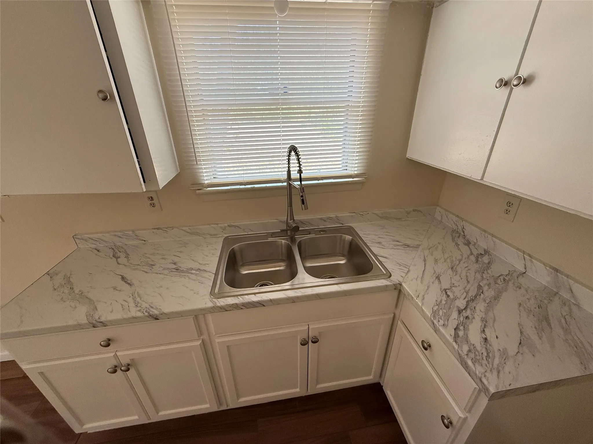 White cabinetry with silver-tone hardware, stainless steel double basin sink, pull-down faucet, and marble-look countertops