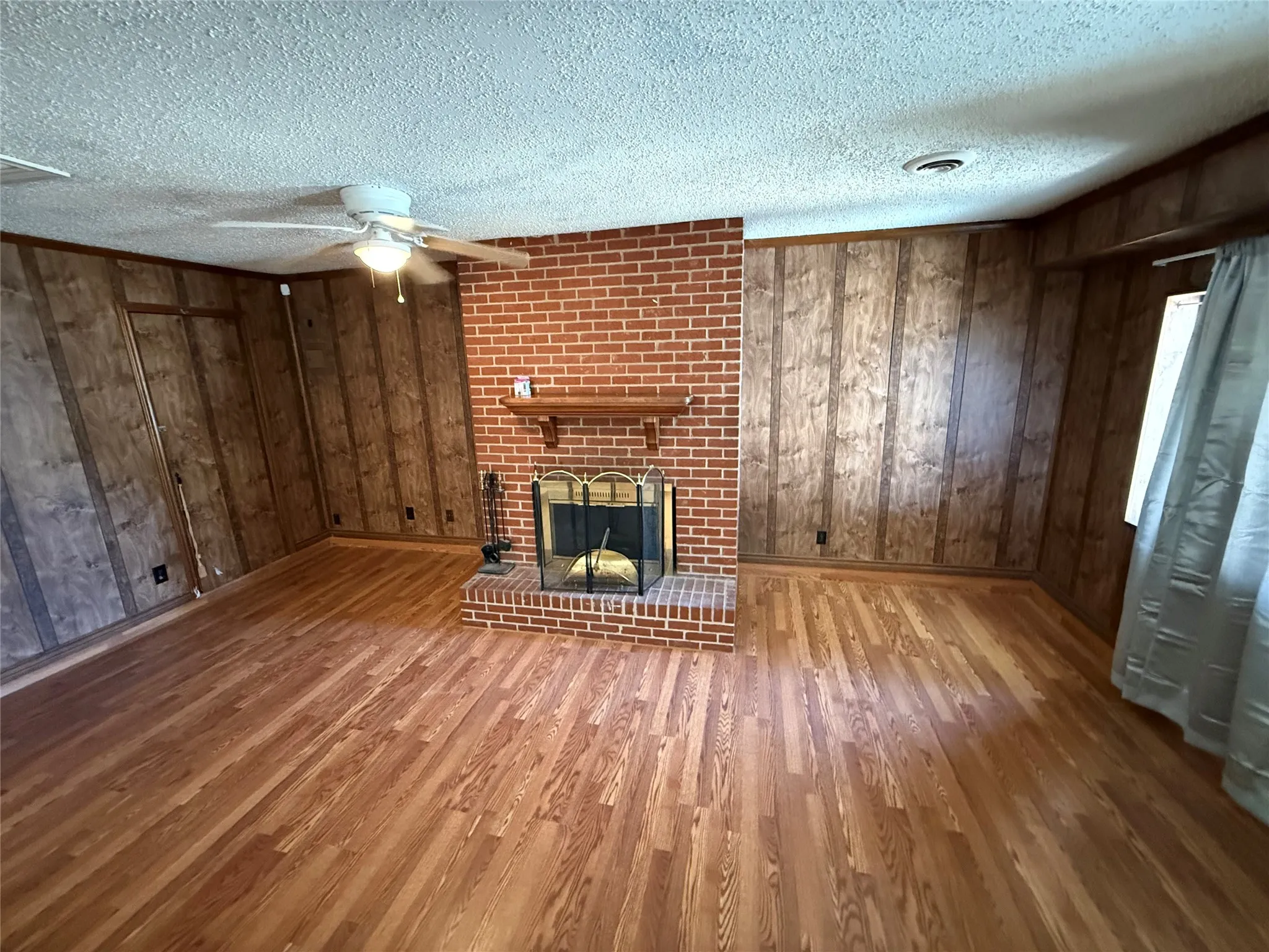 Wood-finish flooring, brick fireplace with mantel, and ceiling fan with integrated lighting