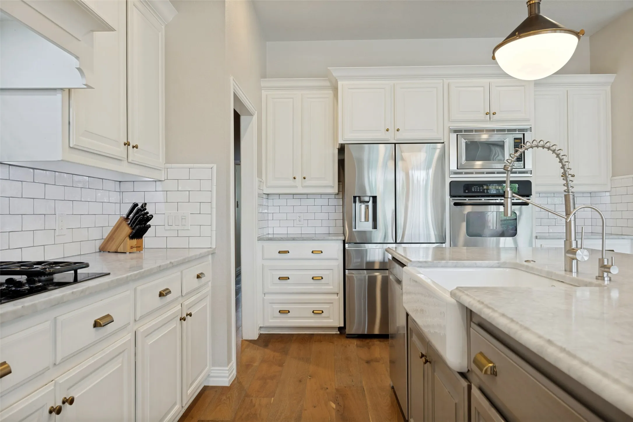 Kitchen featuring white shaker cabinetry, stainless steel appliances, a farmhouse sink, subway tile backsplash, and wood-finish flooring