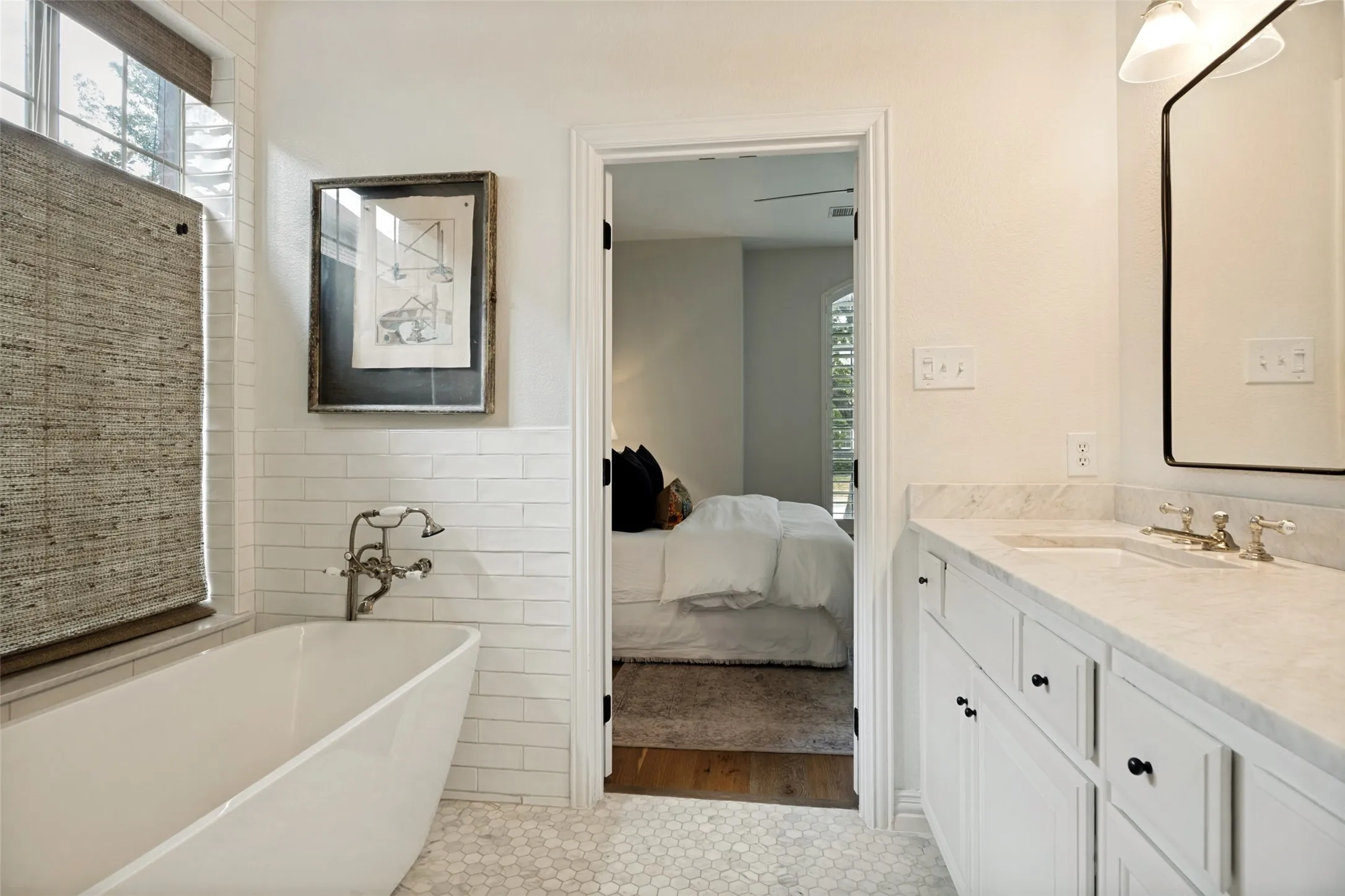 Freestanding soaking tub with wall-mounted faucet, white subway tile wainscoting, hexagon tile flooring, and a single vanity with a stone countertop