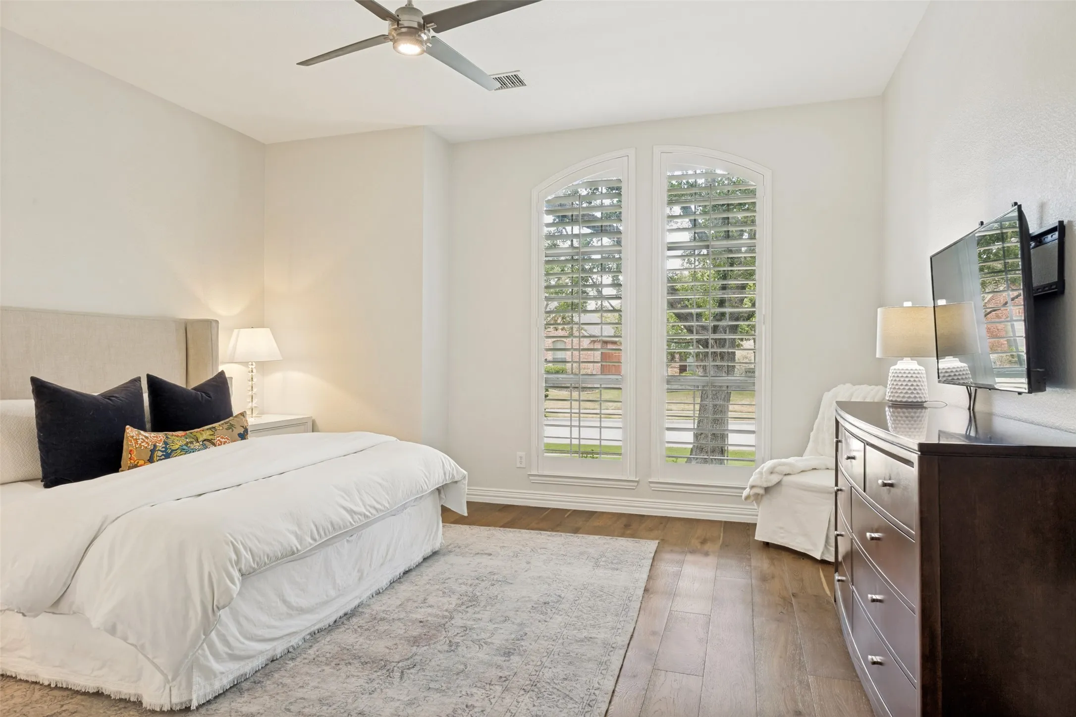 Arched windows with plantation shutters, wood-finish flooring, recessed lighting, ceiling fan, and a neutral color palette