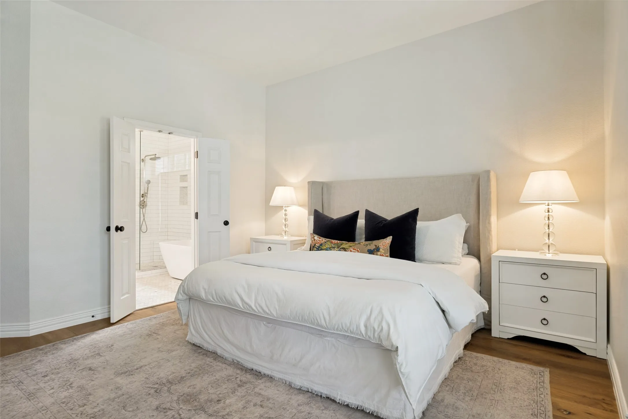 Wood-finish flooring, white walls, and a room with an attached bathroom featuring a standalone tub