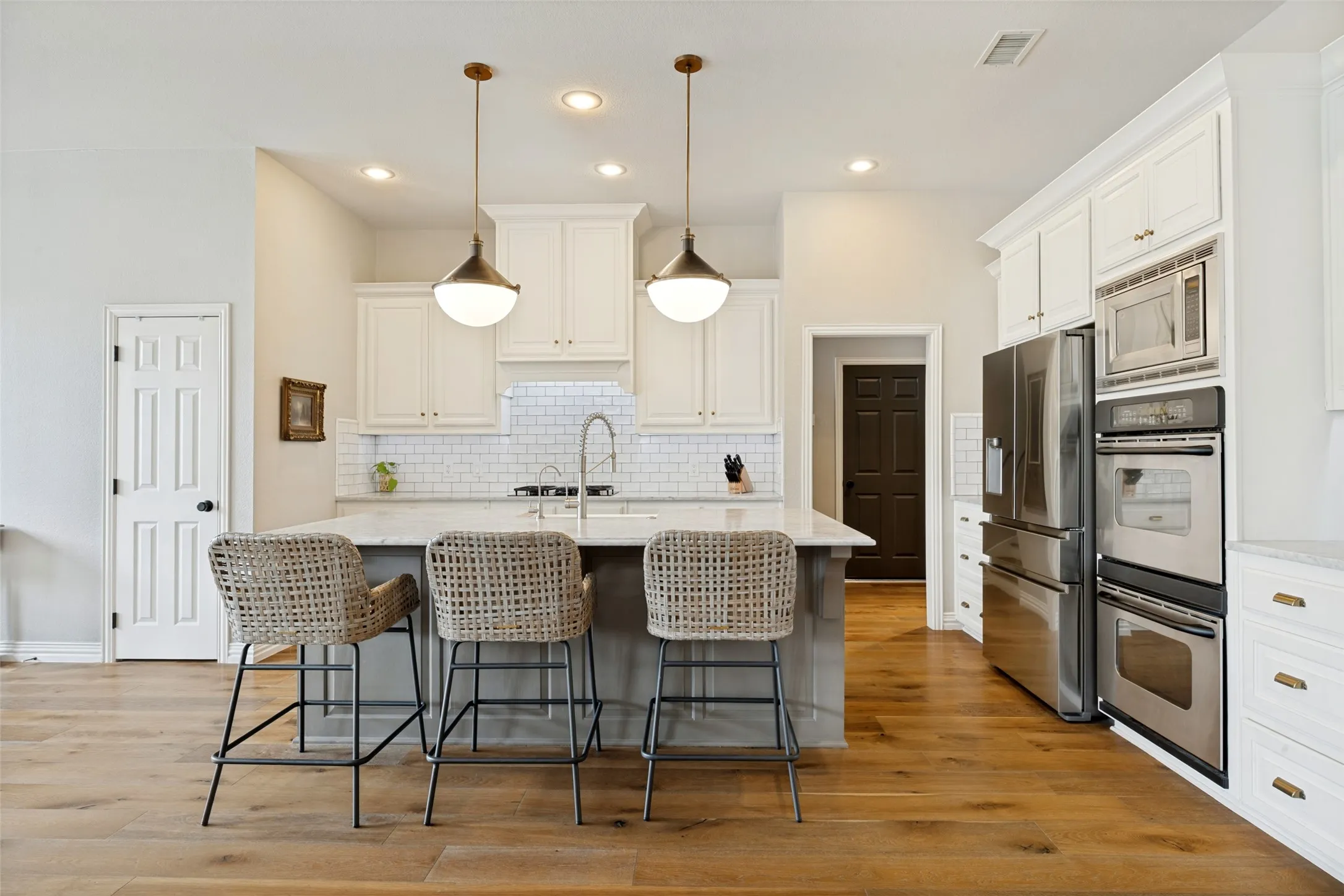 Kitchen featuring wood-finish flooring, white cabinetry, a large kitchen island with seating, stainless steel appliances, and two pendant lights