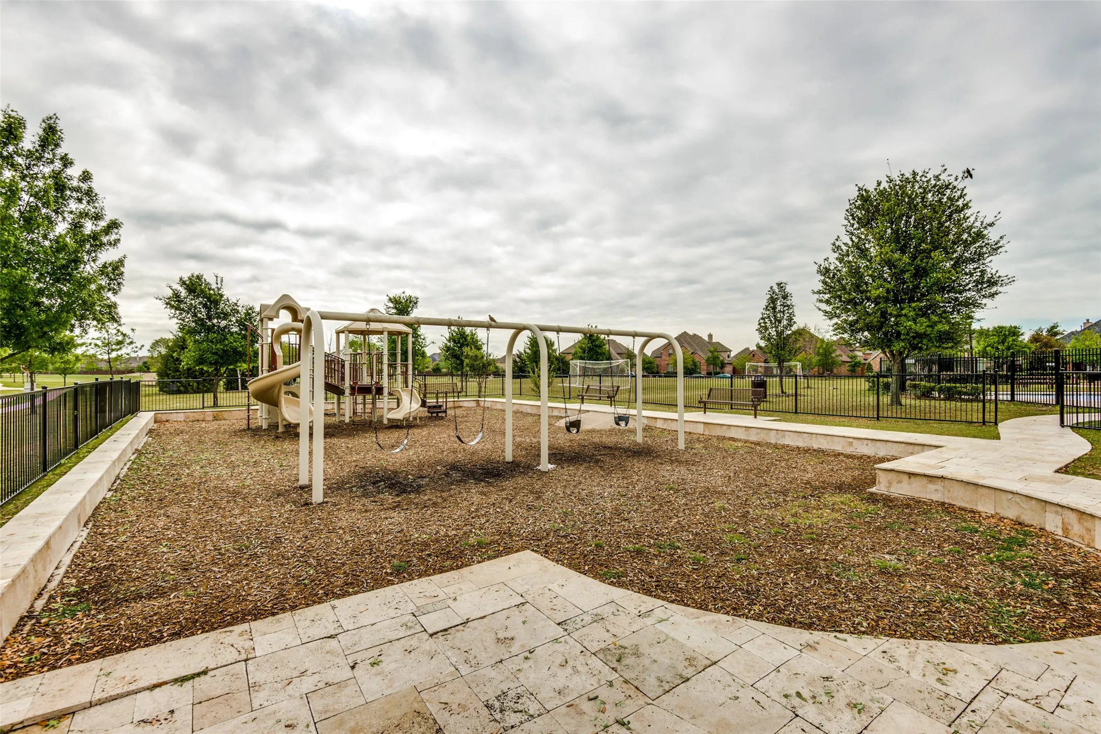 Community playground with multiple slides and swing sets, featuring a wood chip base and surrounding paved pathways