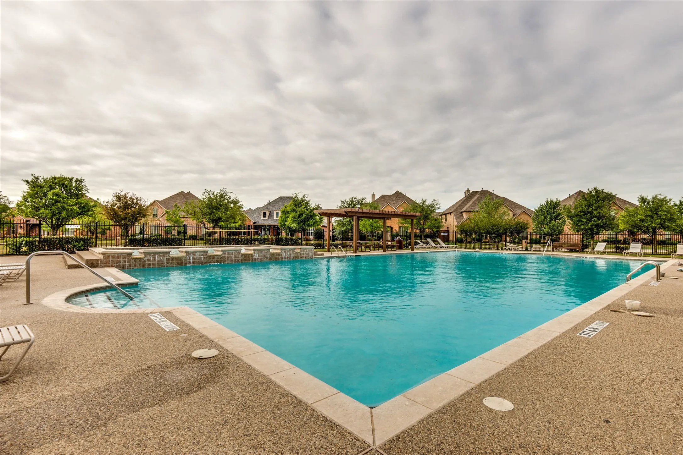 Expansive community swimming pool with an integrated hot tub and stone-look surround