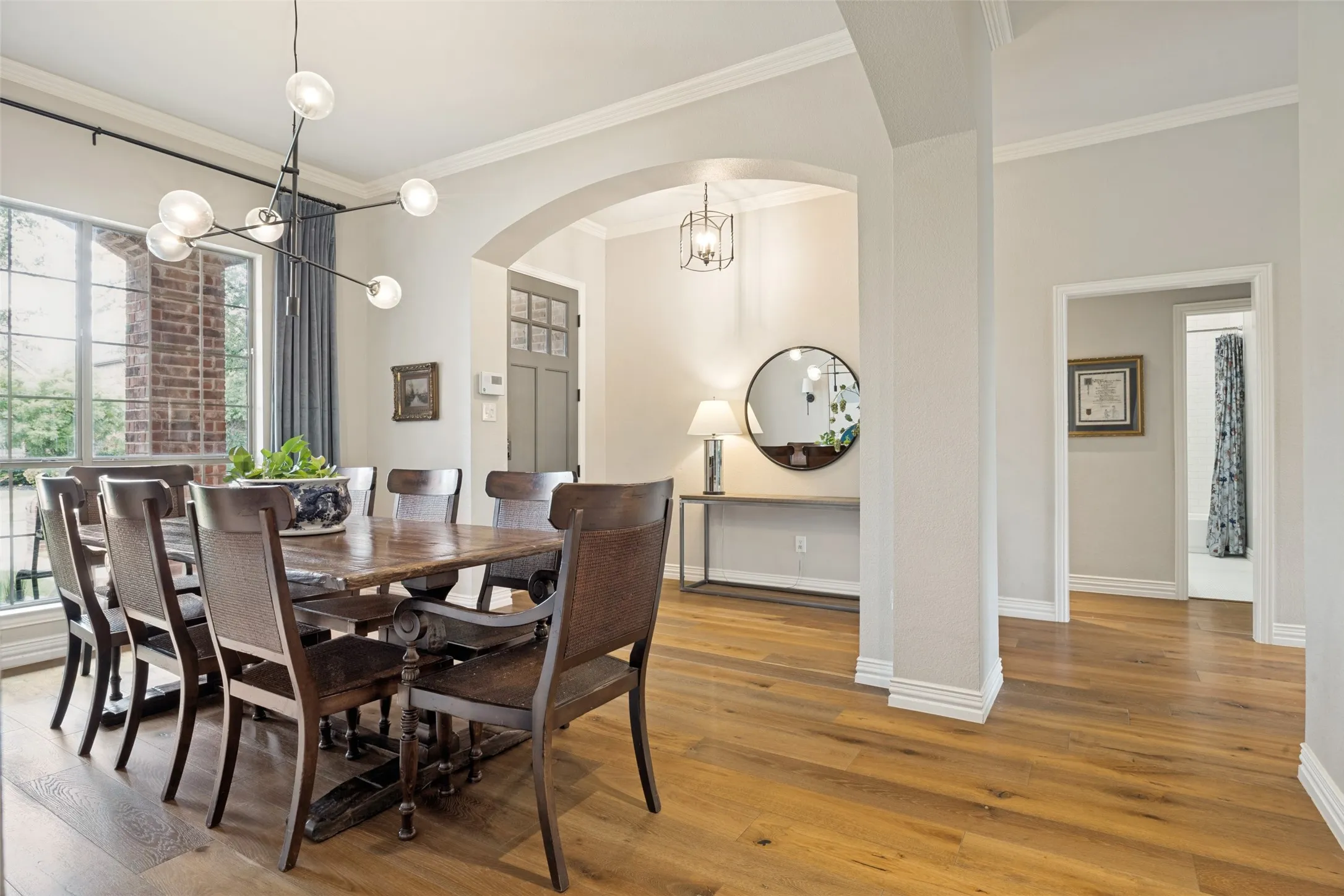 Hardwood flooring throughout, arched entryway, crown molding, modern light fixture, and brick exterior accents