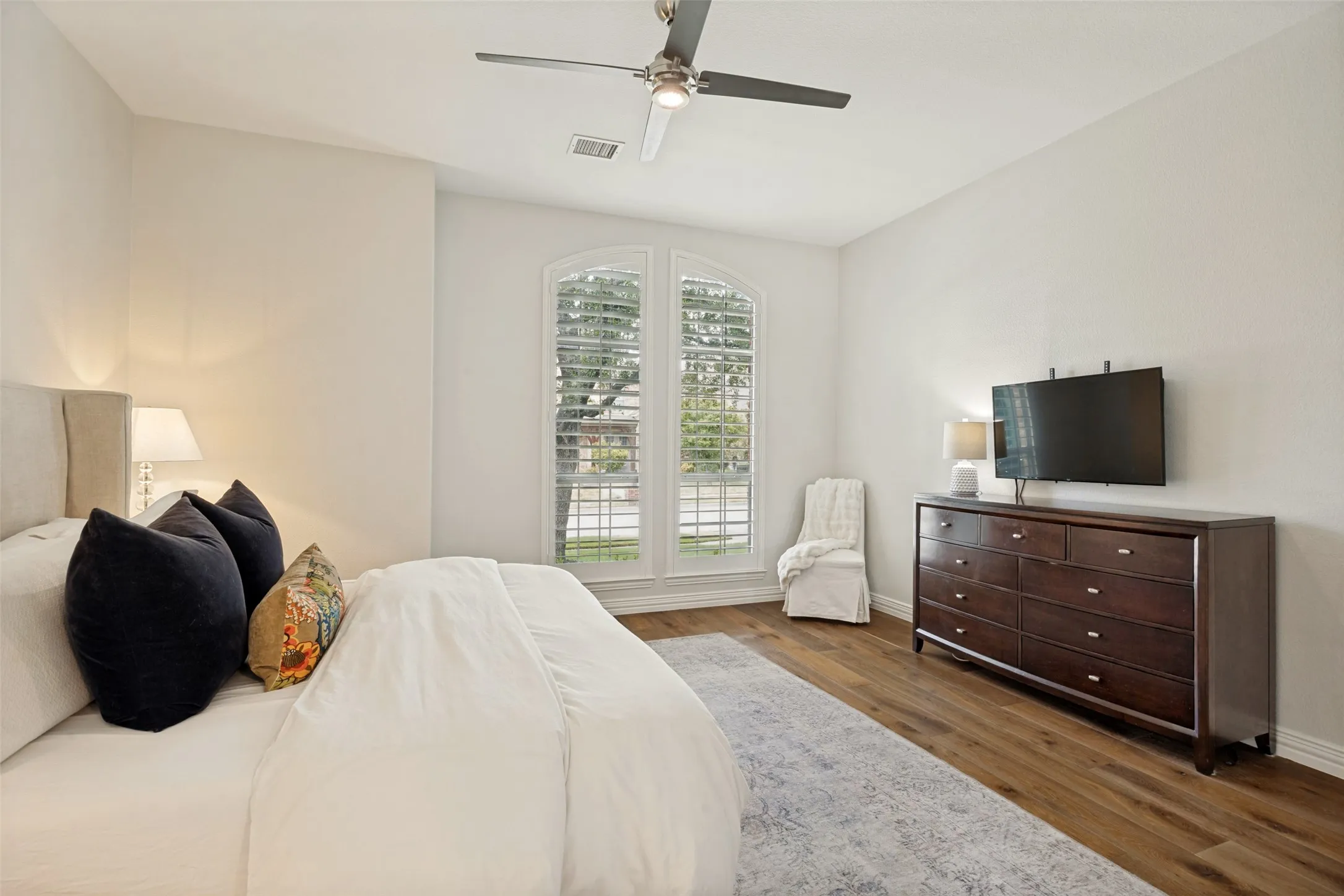 Vaulted ceilings with a ceiling fan, arched windows, plantation shutters, and wood-finish flooring