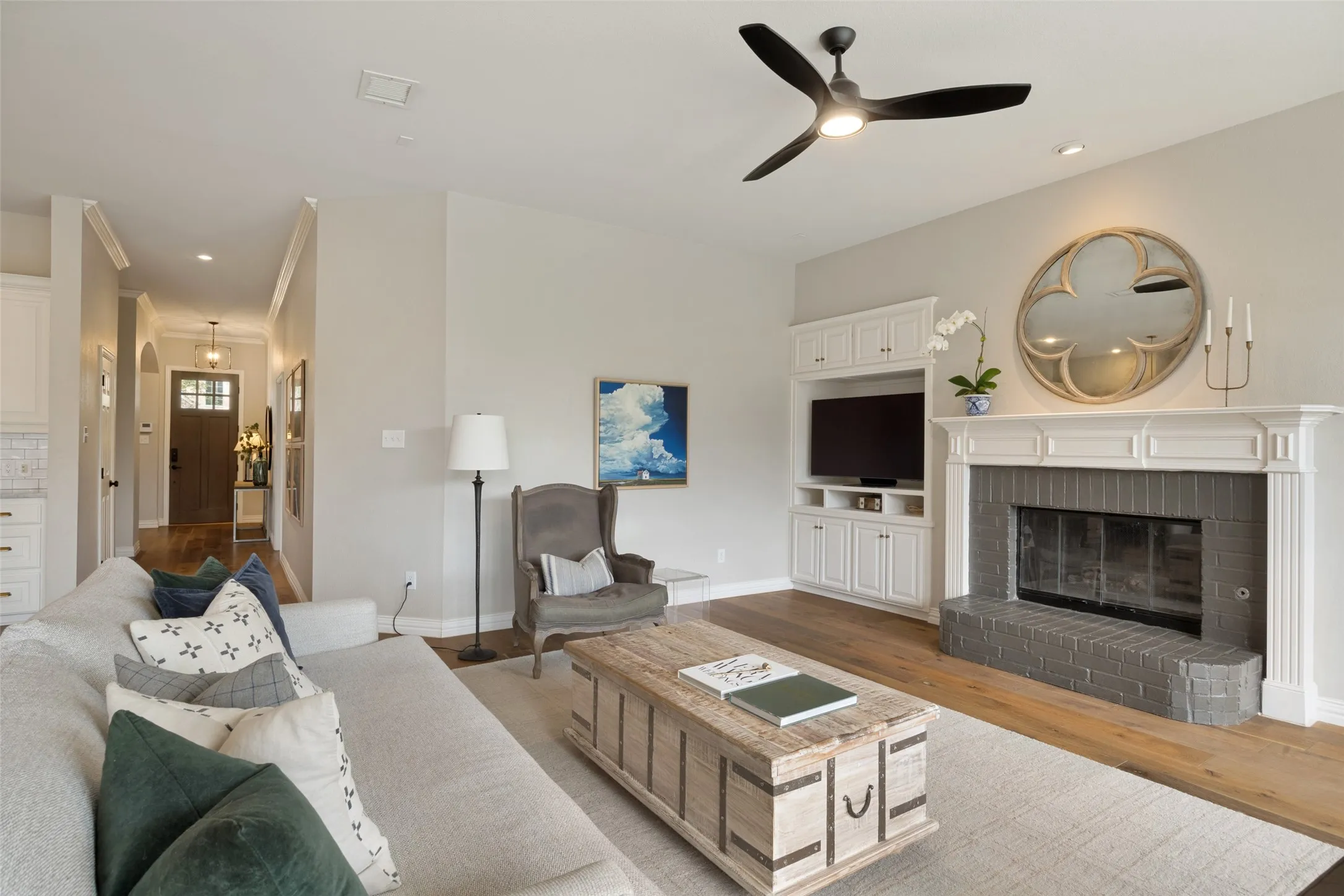 Spacious living area featuring wood-finish flooring, a contemporary ceiling fan, and a fireplace with a white mantel and gray brick surround