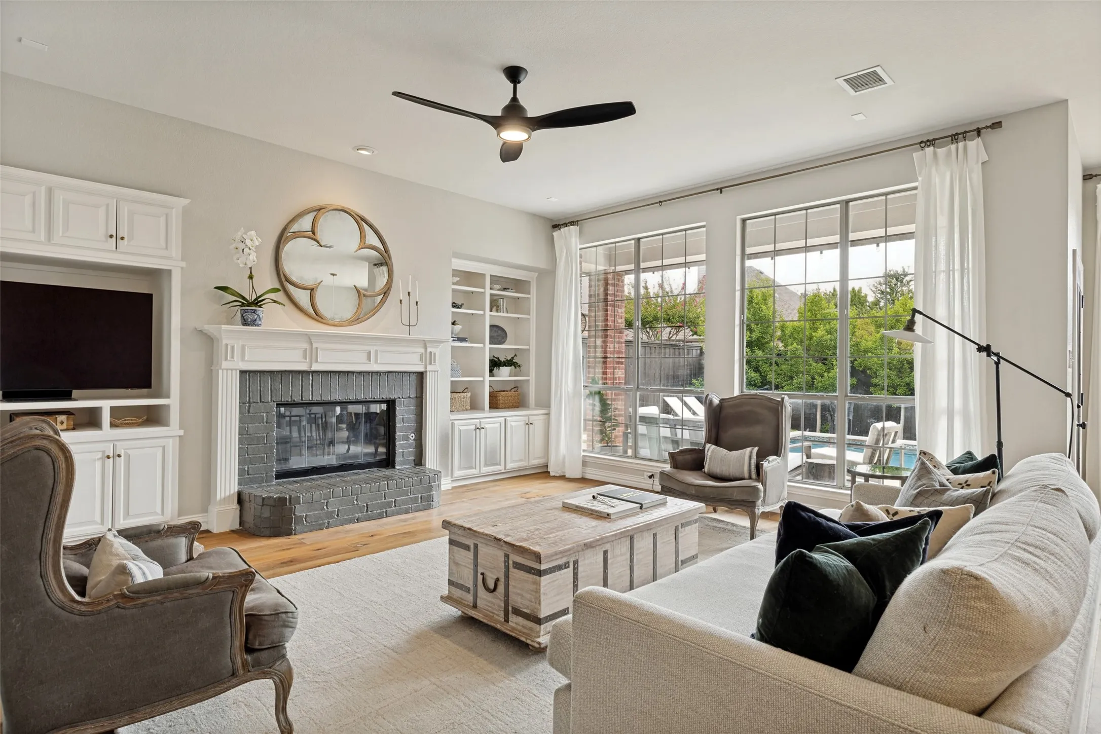 Spacious living area featuring a gray brick fireplace with a white mantel, built-in cabinetry, wood-finish flooring, and large windows