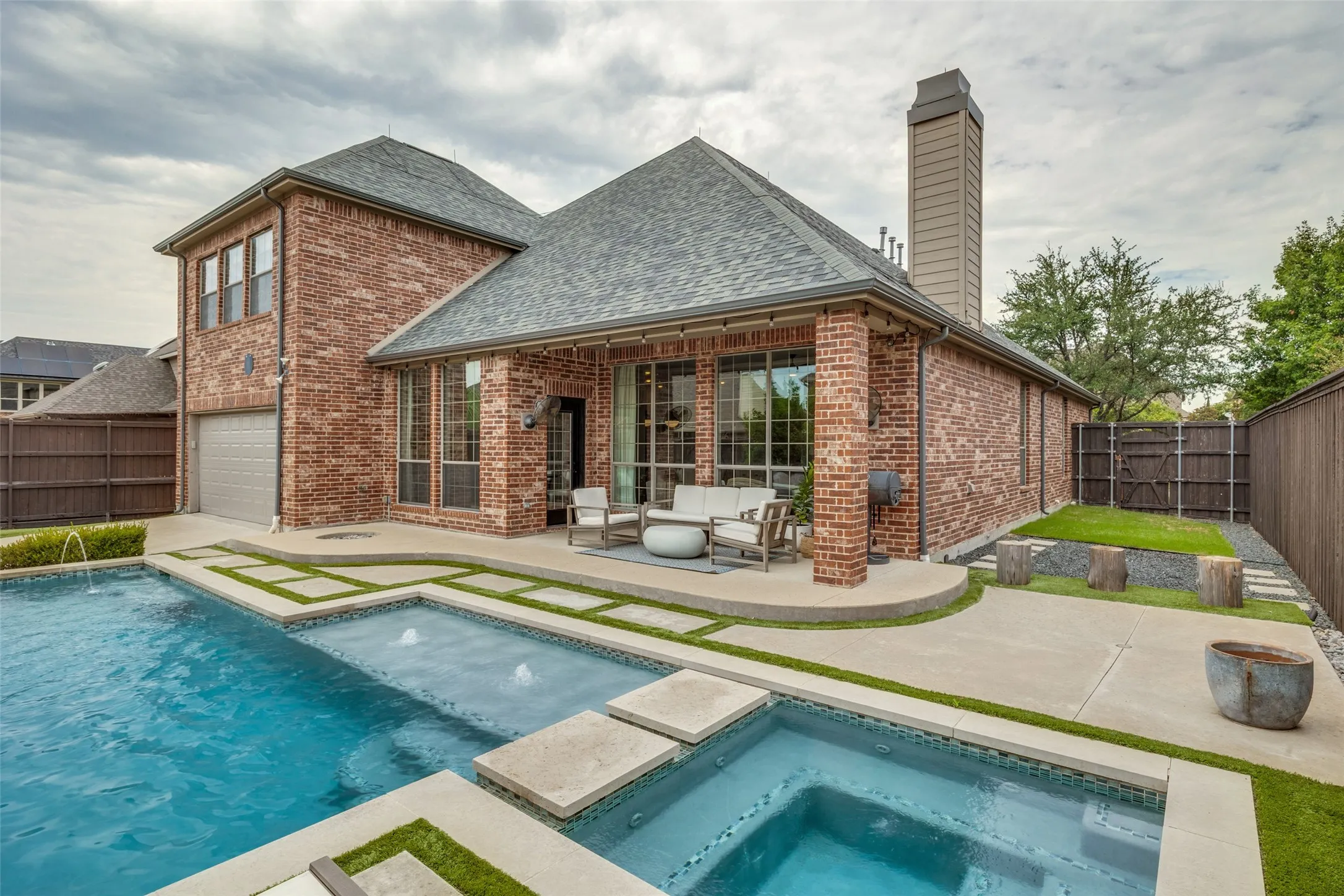 Brick exterior with a multi-level pool, attached spa, and an integrated patio