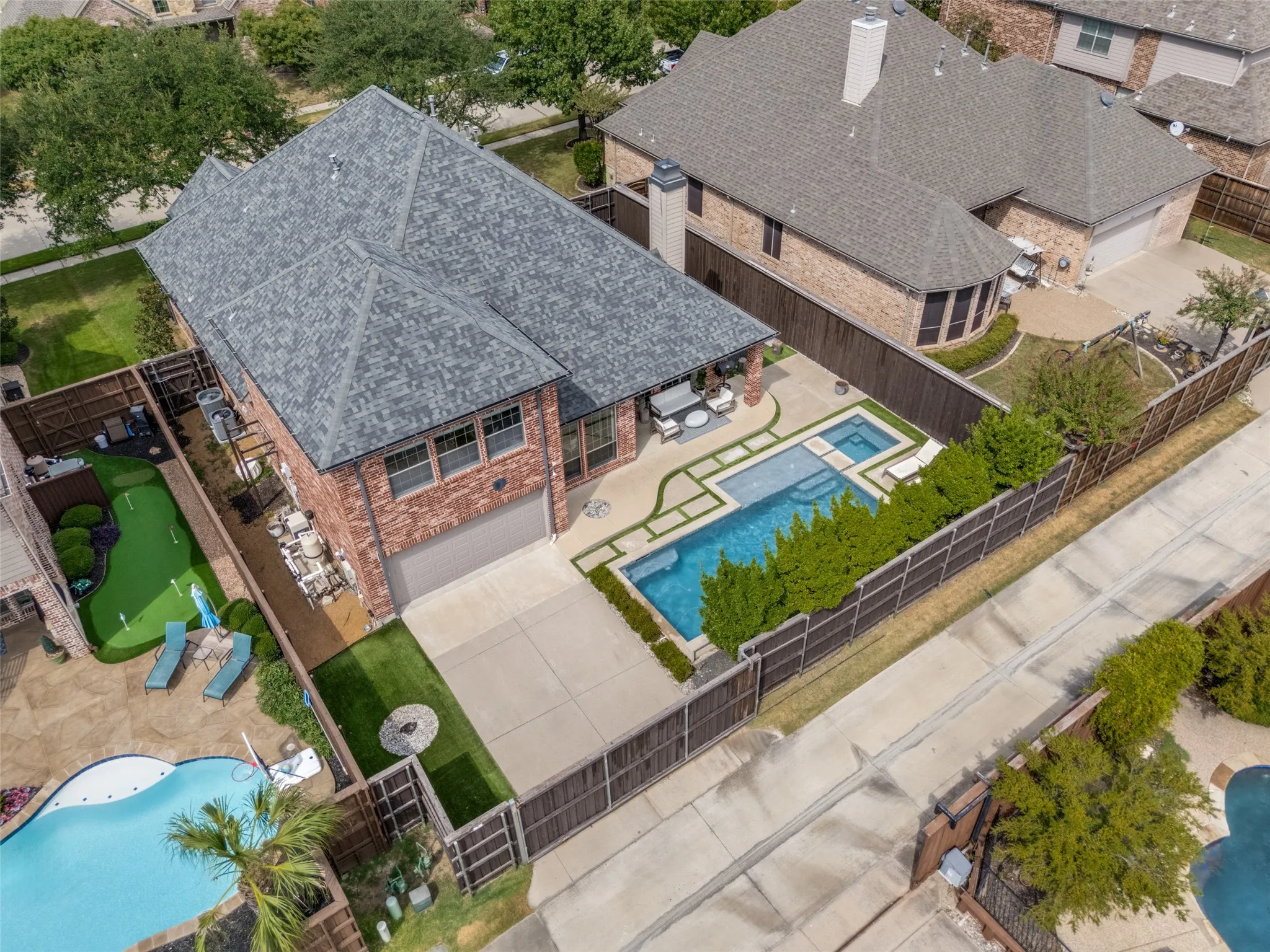 Brick exterior with an attached garage, featuring a private swimming pool with integrated spa, a dedicated putting green, and a covered patio