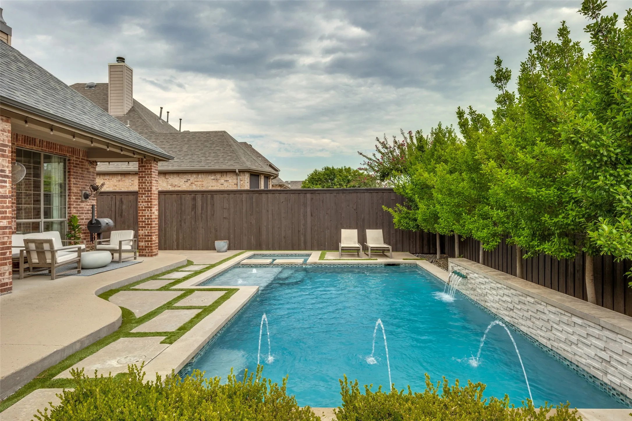 Outdoor living area featuring a covered patio, swimming pool with water features, integrated spa, and a privacy fence