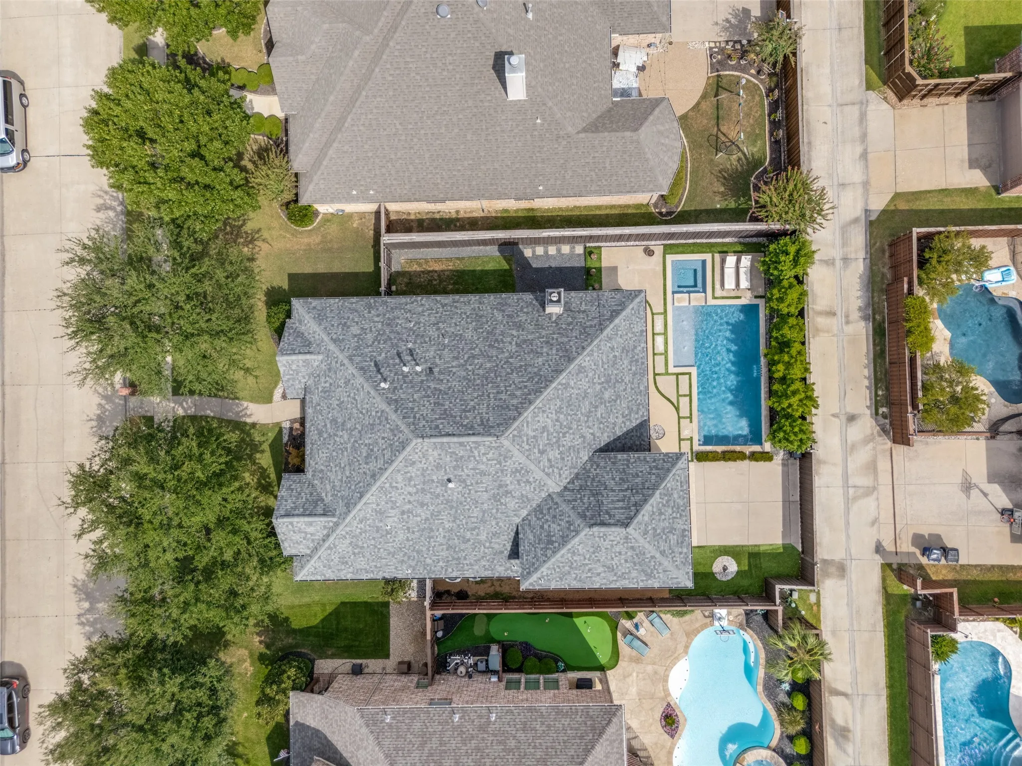 Shingled roof residence featuring a rectangular swimming pool, integrated spa, concrete patio, and a putting green