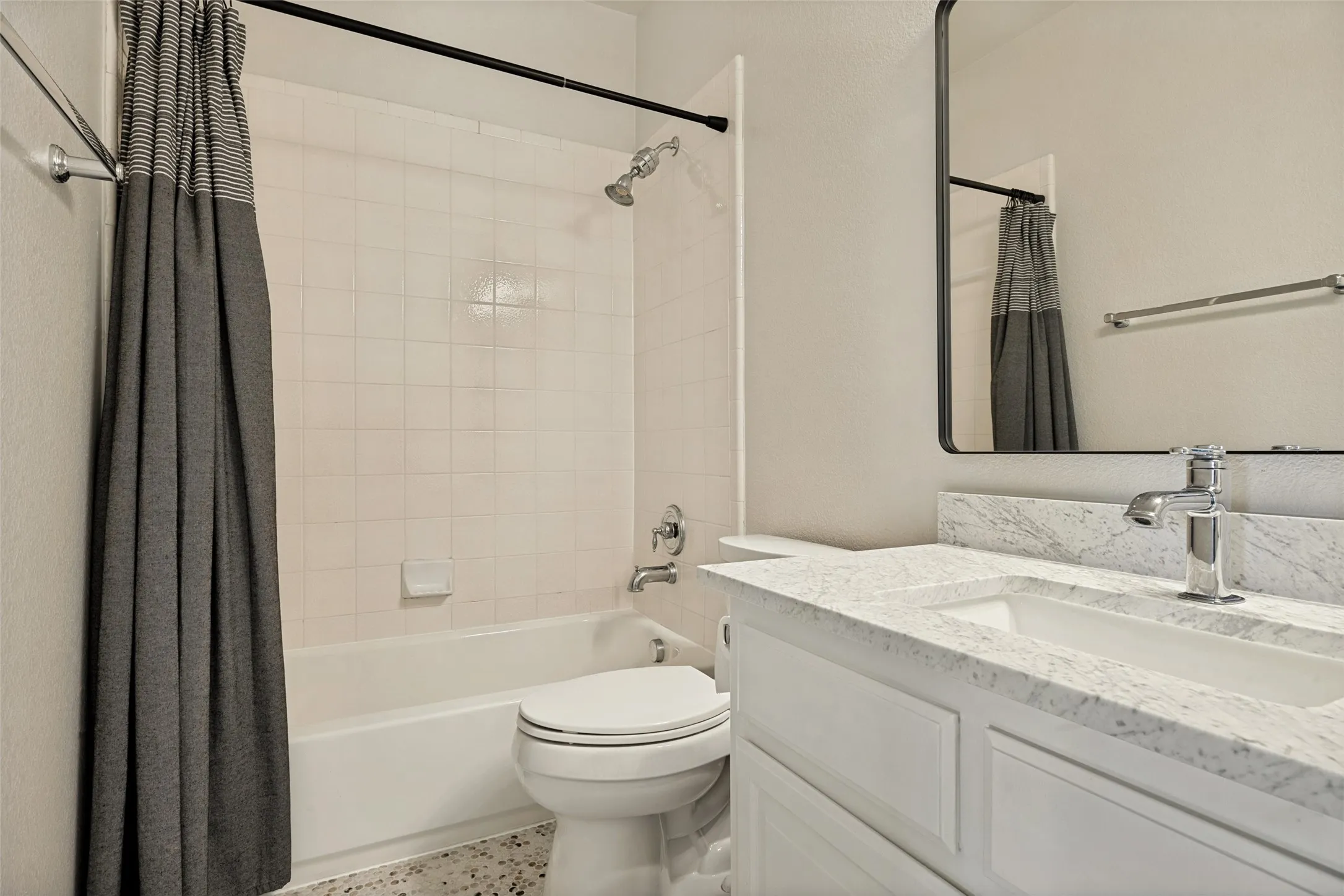Bathroom featuring a white vanity with a light-toned countertop, an integrated sink, a rectangular mirror, and a shower-over-tub combination with white tile surround