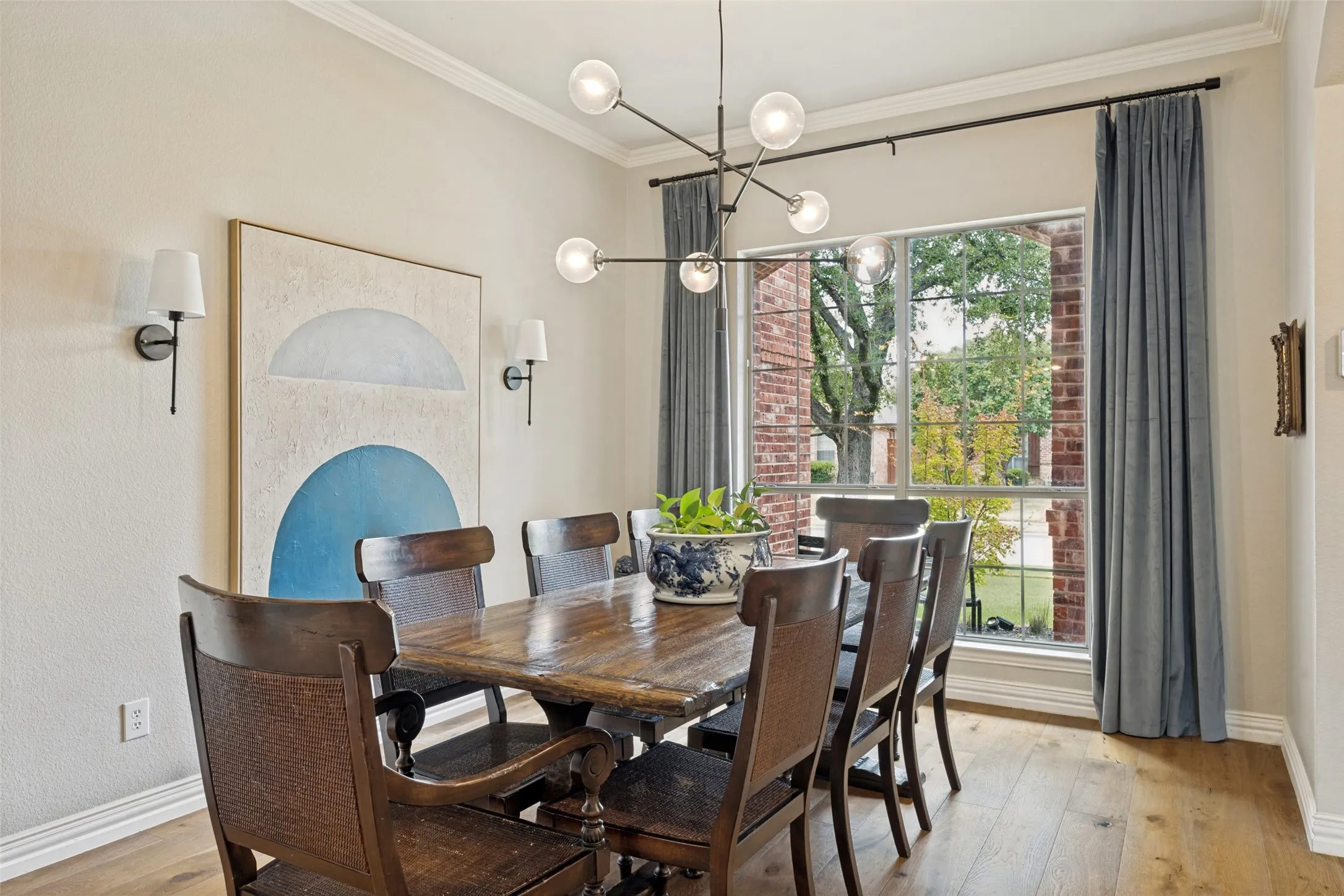 Wood-finish flooring, crown molding, modern chandelier, double-hung window, and wall sconces