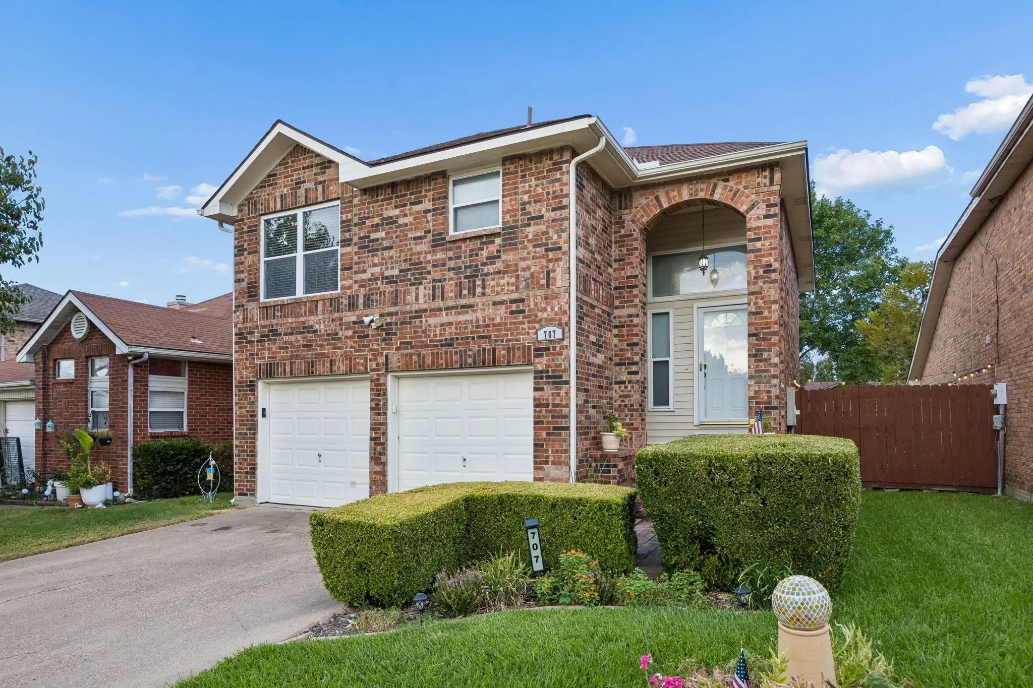 Brick facade, arched entry, two-car garage, manicured shrubs, and a concrete driveway