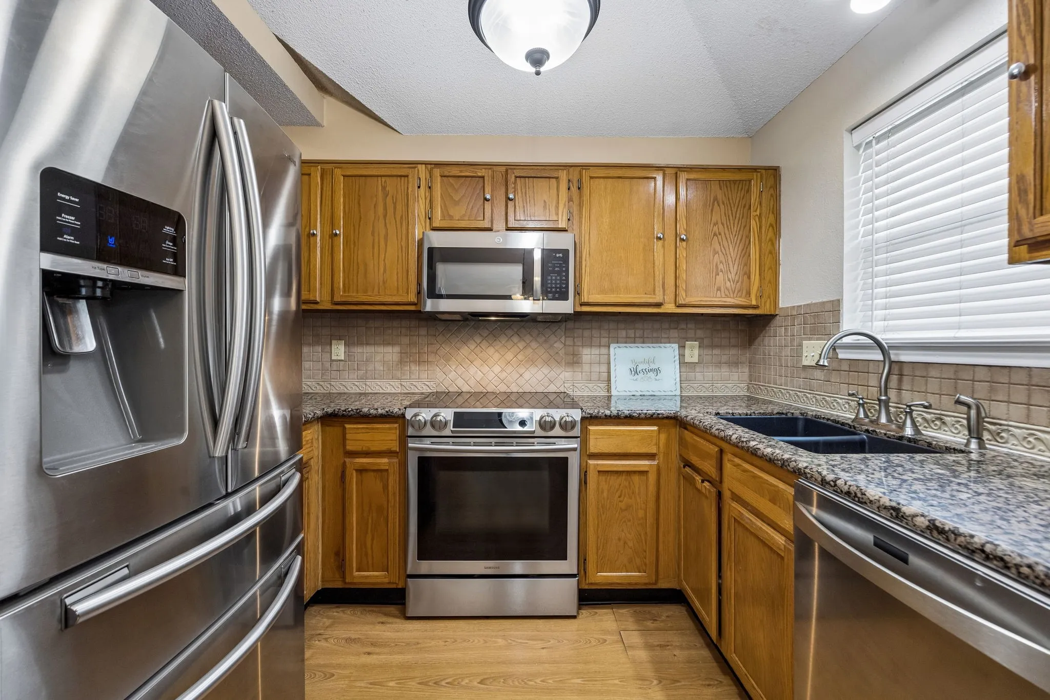 Kitchen featuring wood-finish flooring, oak cabinetry, stainless steel appliances, granite countertops, and a tile backsplash