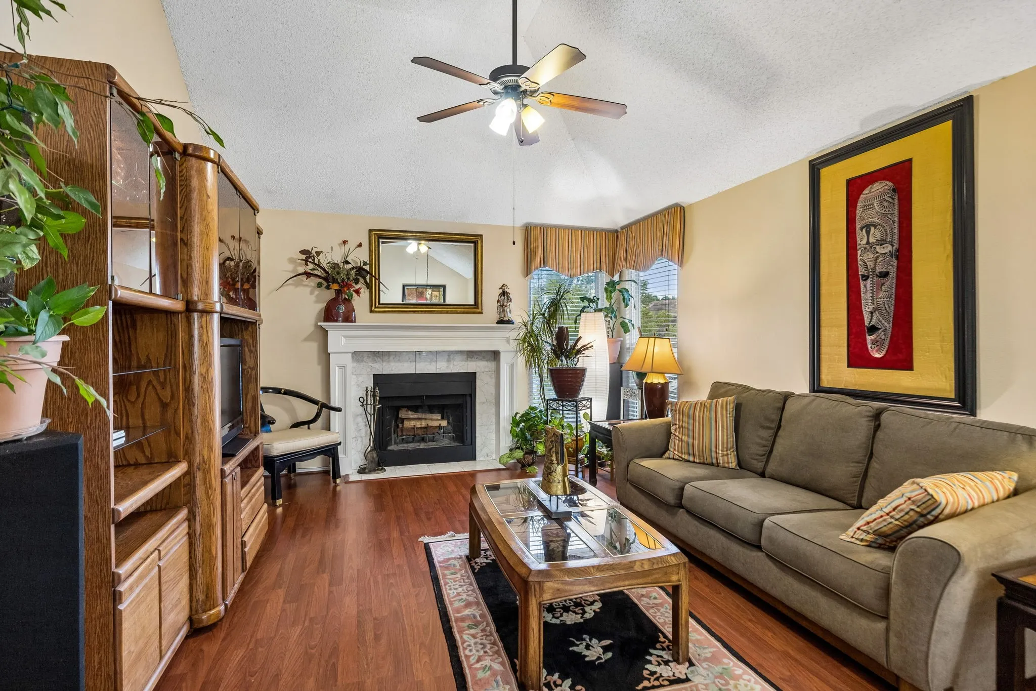 Vaulted ceiling featuring a ceiling fan, fireplace with a tile surround and white mantel, and wood-finish flooring