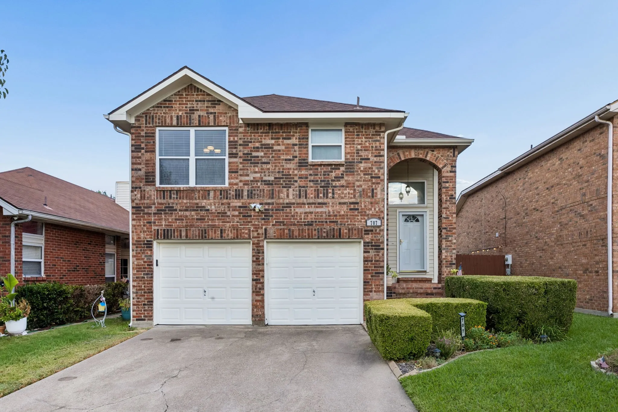 Brick exterior with arched entryway, two-car garage, and concrete driveway