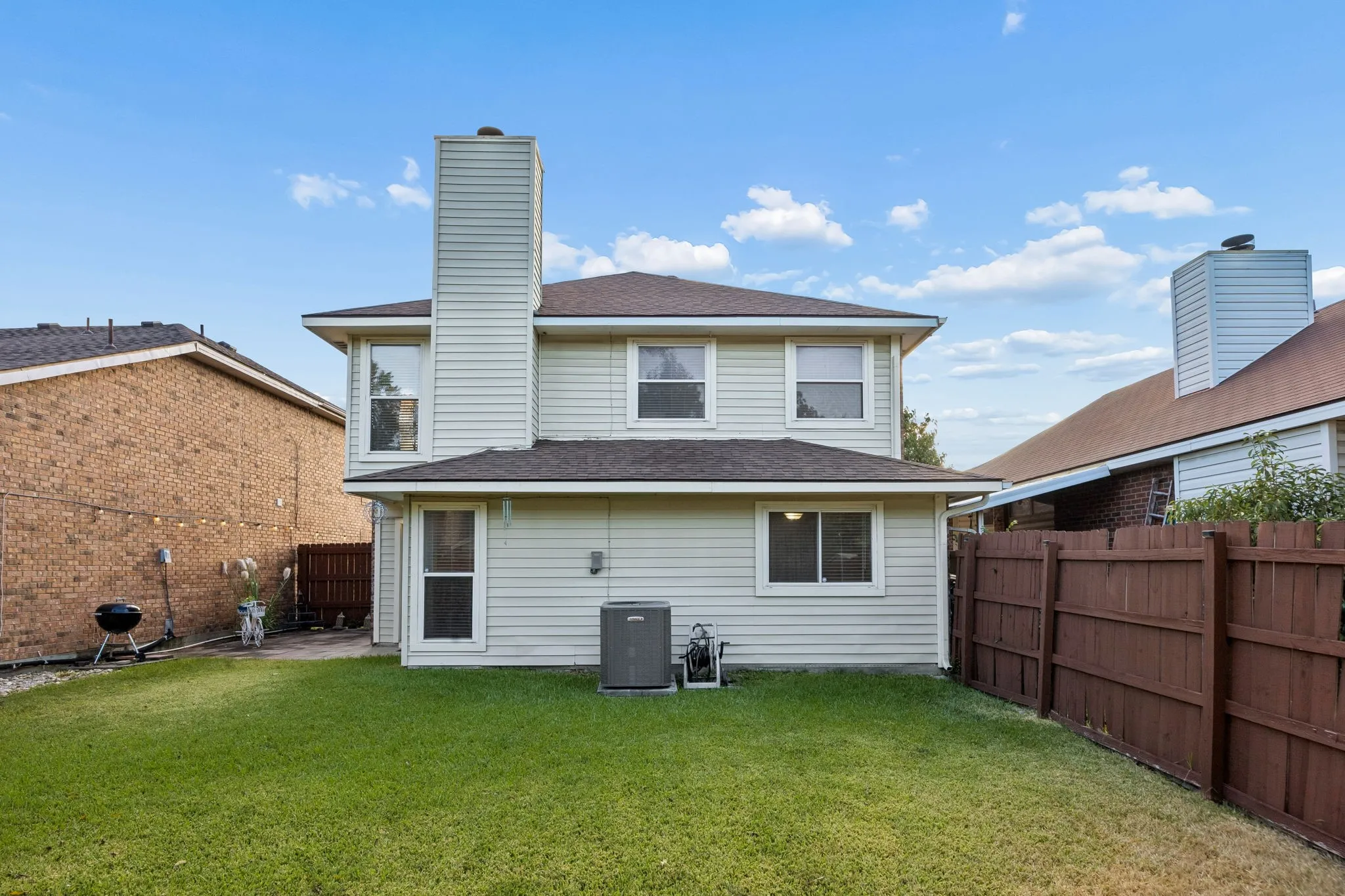 Expansive green lawn, two-story structure, light-colored siding, dark shingle roof, and a privacy fence