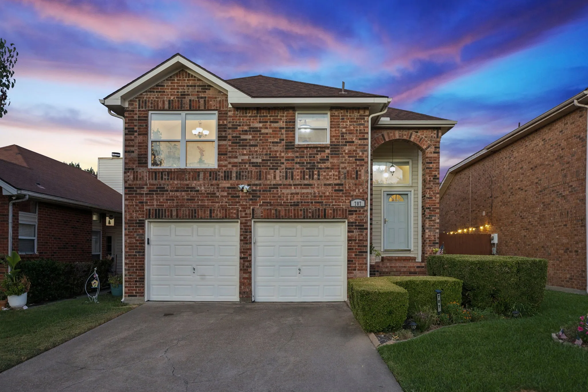 Brick exterior featuring a two-car garage, concrete driveway, and arched entryway with a paneled door