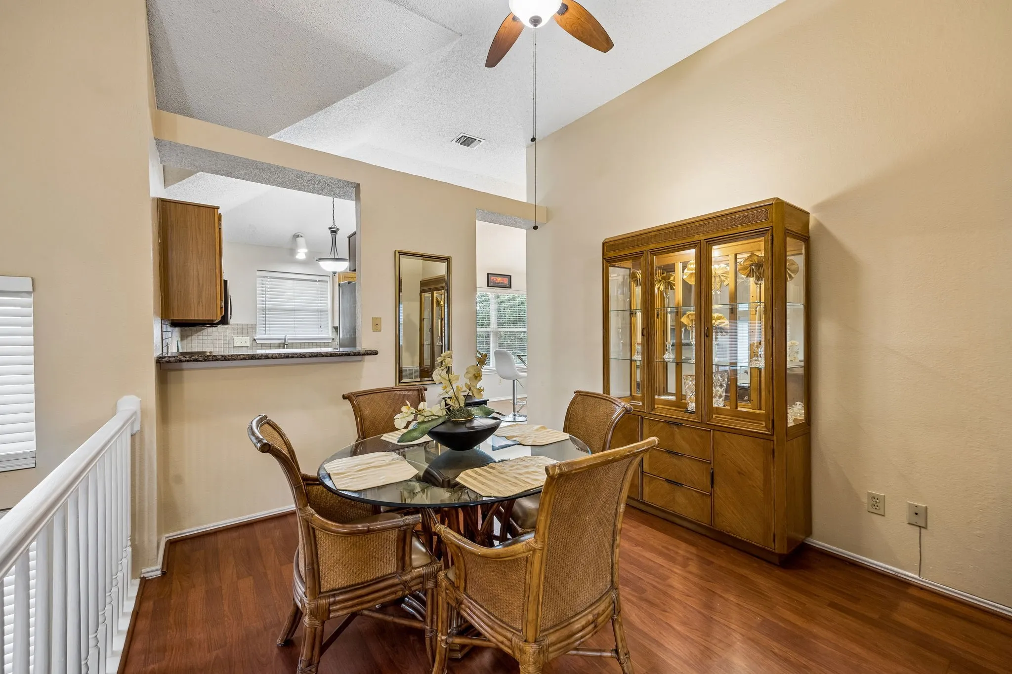 Wood-finish flooring throughout, vaulted ceiling with a ceiling fan, and a kitchen pass-through with a stone-finish countertop and tile backsplash