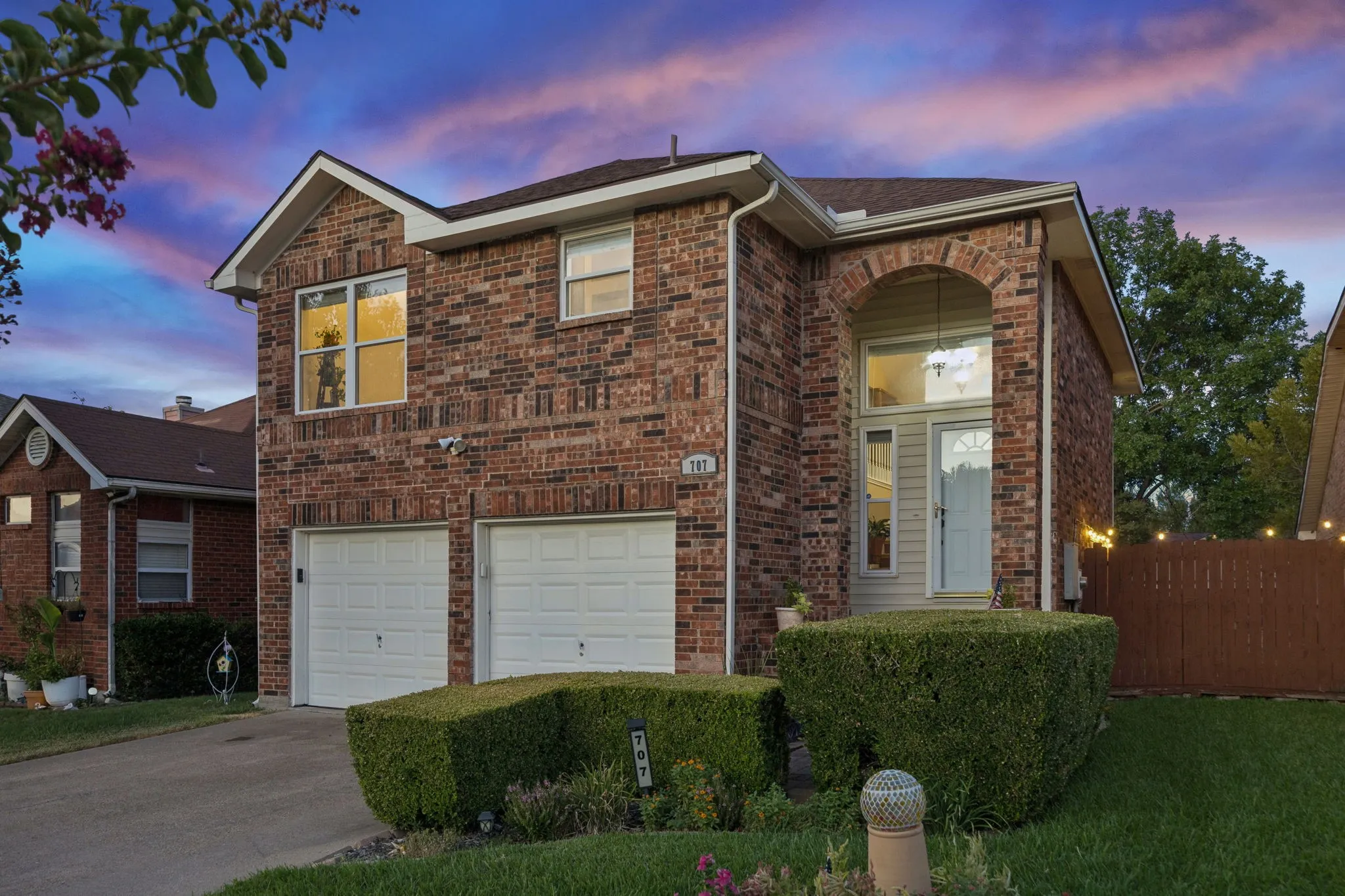 Brick exterior featuring an arched entry, two-car garage, and landscaped front yard