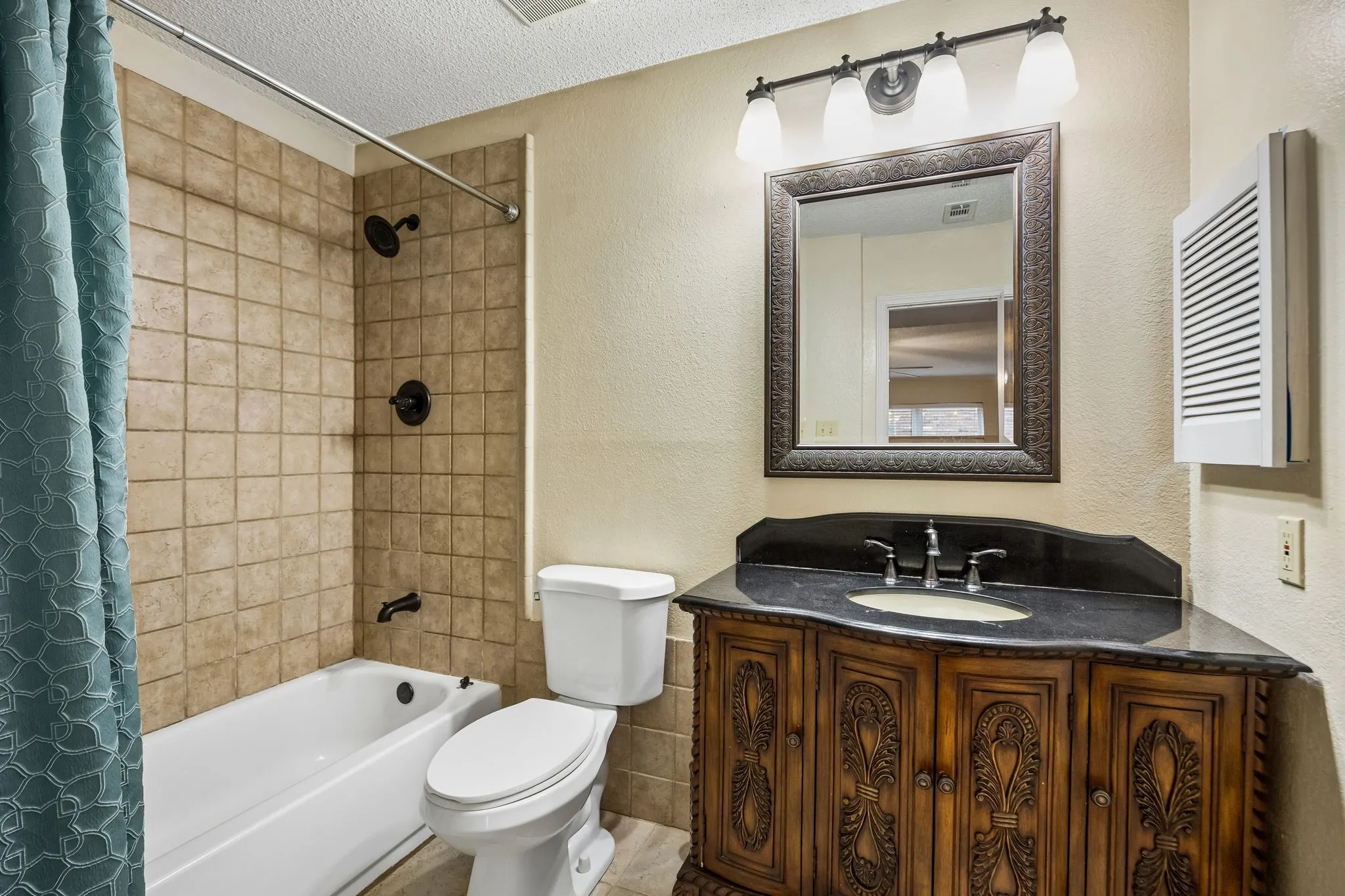 Bathroom featuring a built-in tub with tile surround, a dark wood-finish vanity with an integrated sink, a dark countertop, and an ornate framed mirror