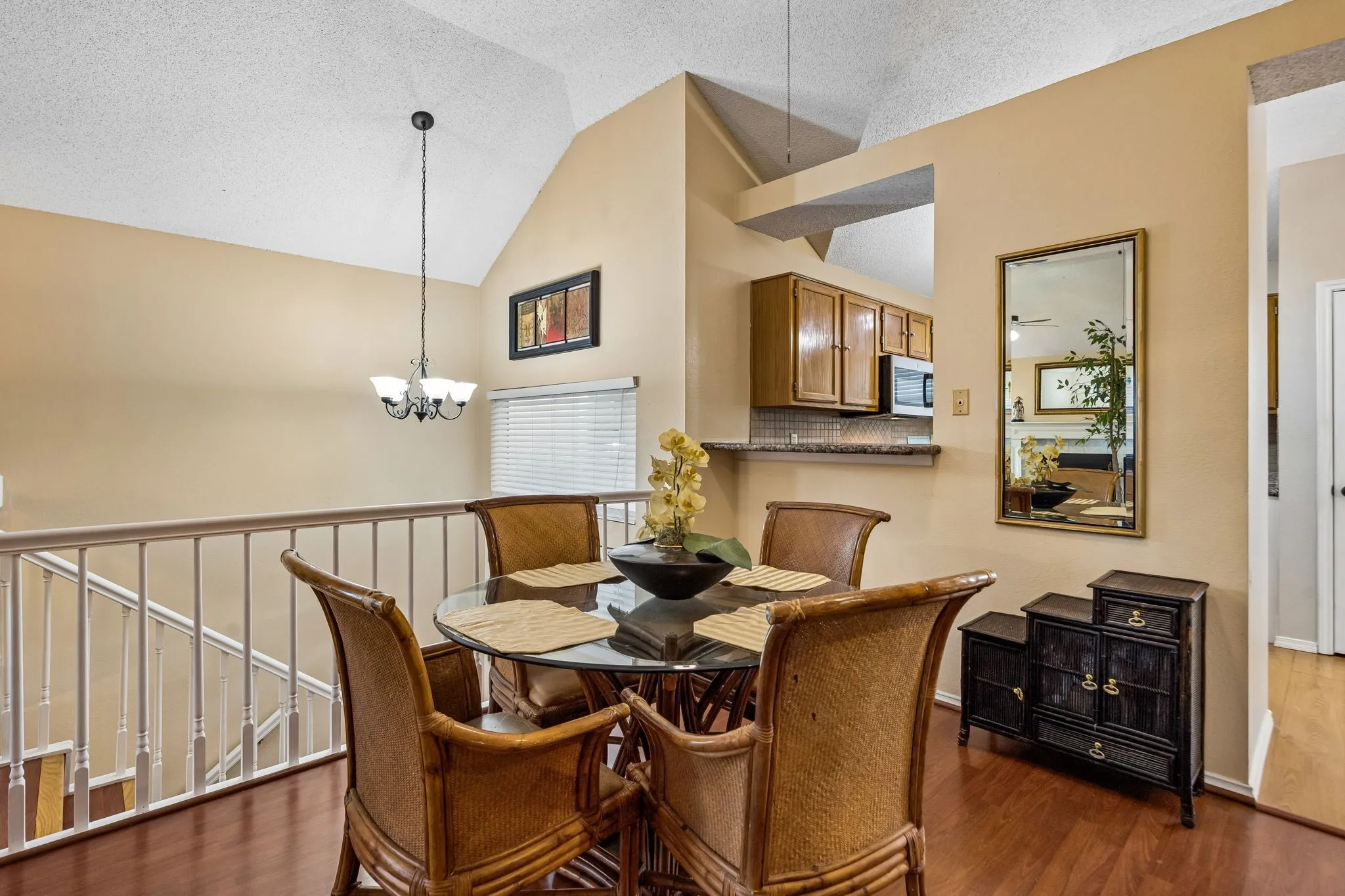 Vaulted ceiling with an attached chandelier, wood-finish flooring, and built-in kitchen cabinetry with a stainless steel microwave