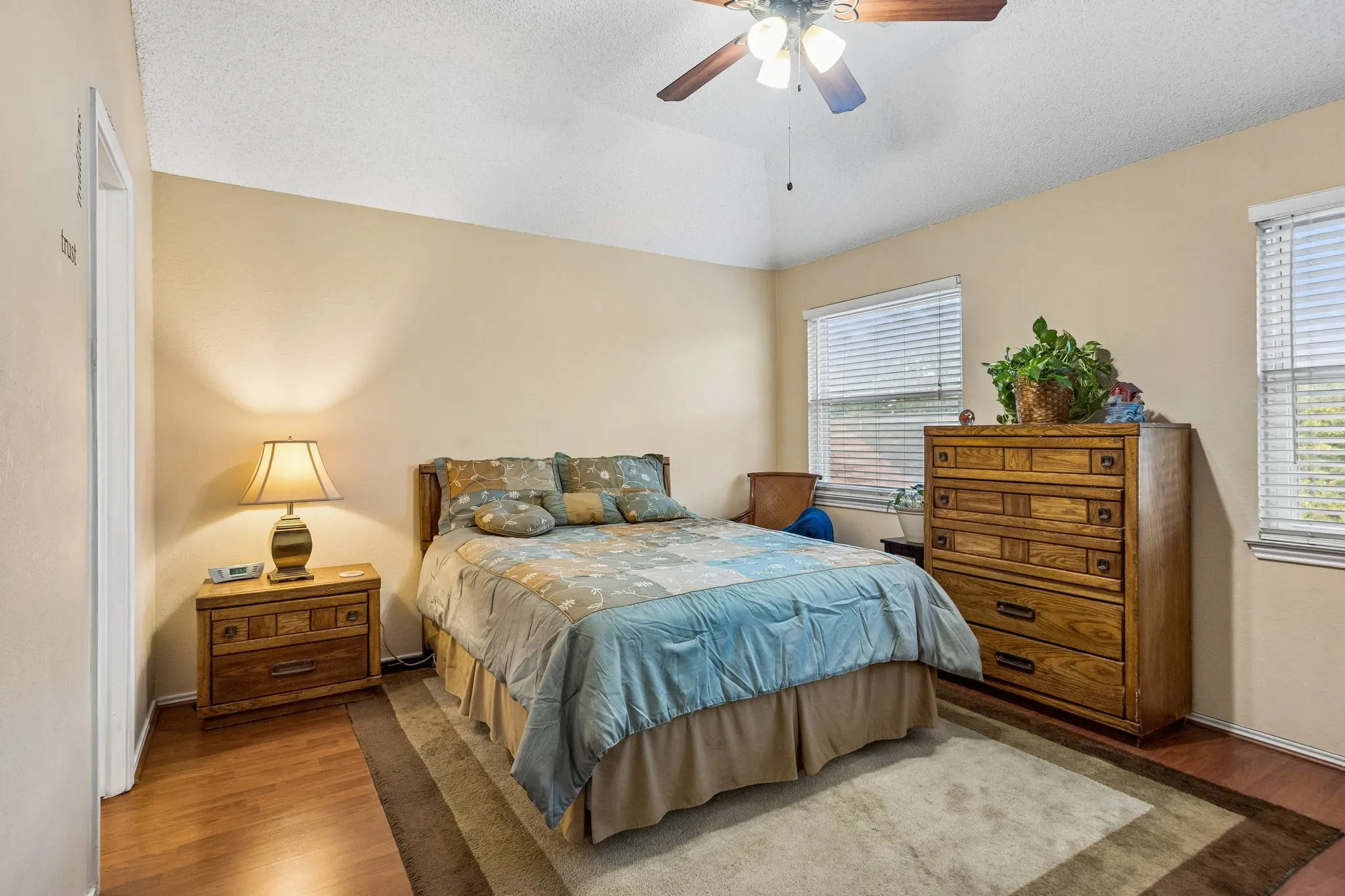 Vaulted ceiling with a ceiling fan, wood-finish flooring, and multiple windows with blinds