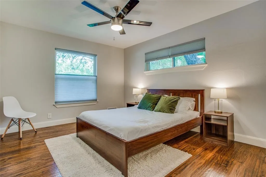 Wood-finish flooring, two windows with blinds, and a ceiling fan with integrated lighting