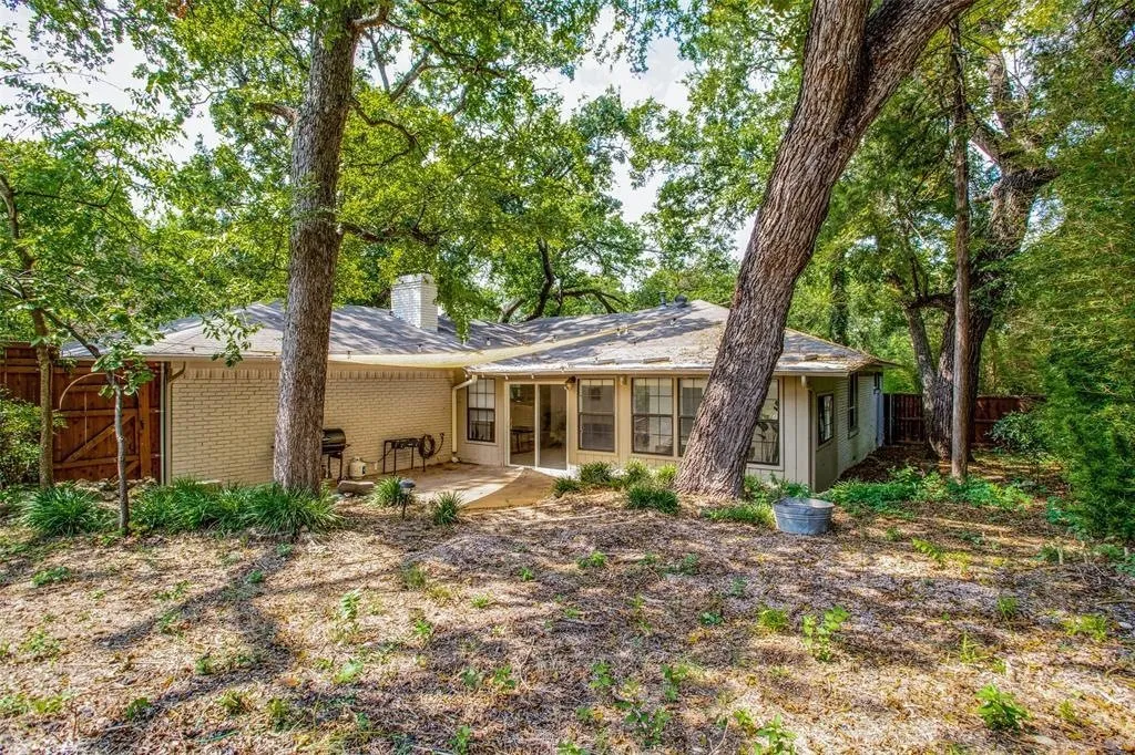 Expansive backyard featuring mature trees, a brick exterior, a sunroom with multiple windows, a patio, and a privacy fence