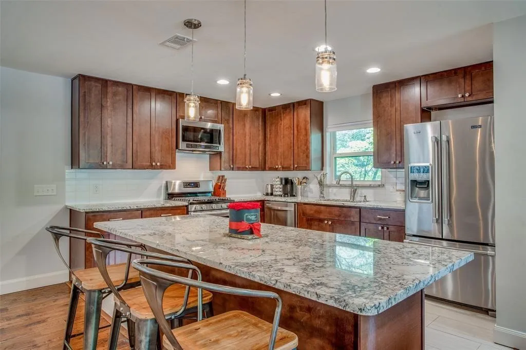 Kitchen featuring a large island with a stone-finish countertop, wood cabinetry, stainless steel appliances, and pendant lighting