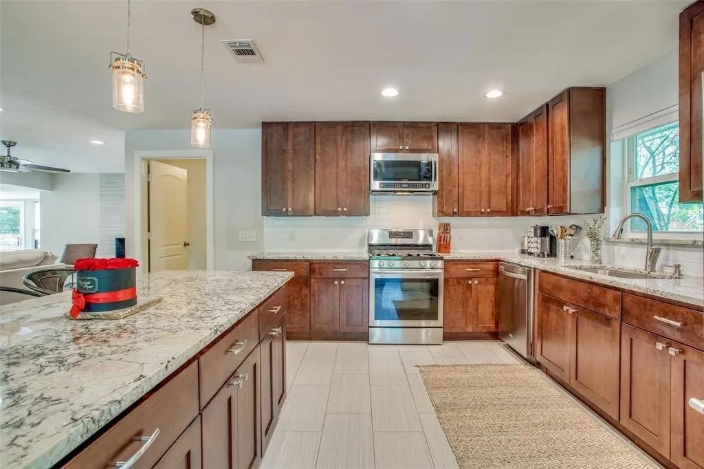 Kitchen featuring wood cabinetry, light-toned countertops, white subway tile backsplash, stainless steel appliances, and pendant lighting