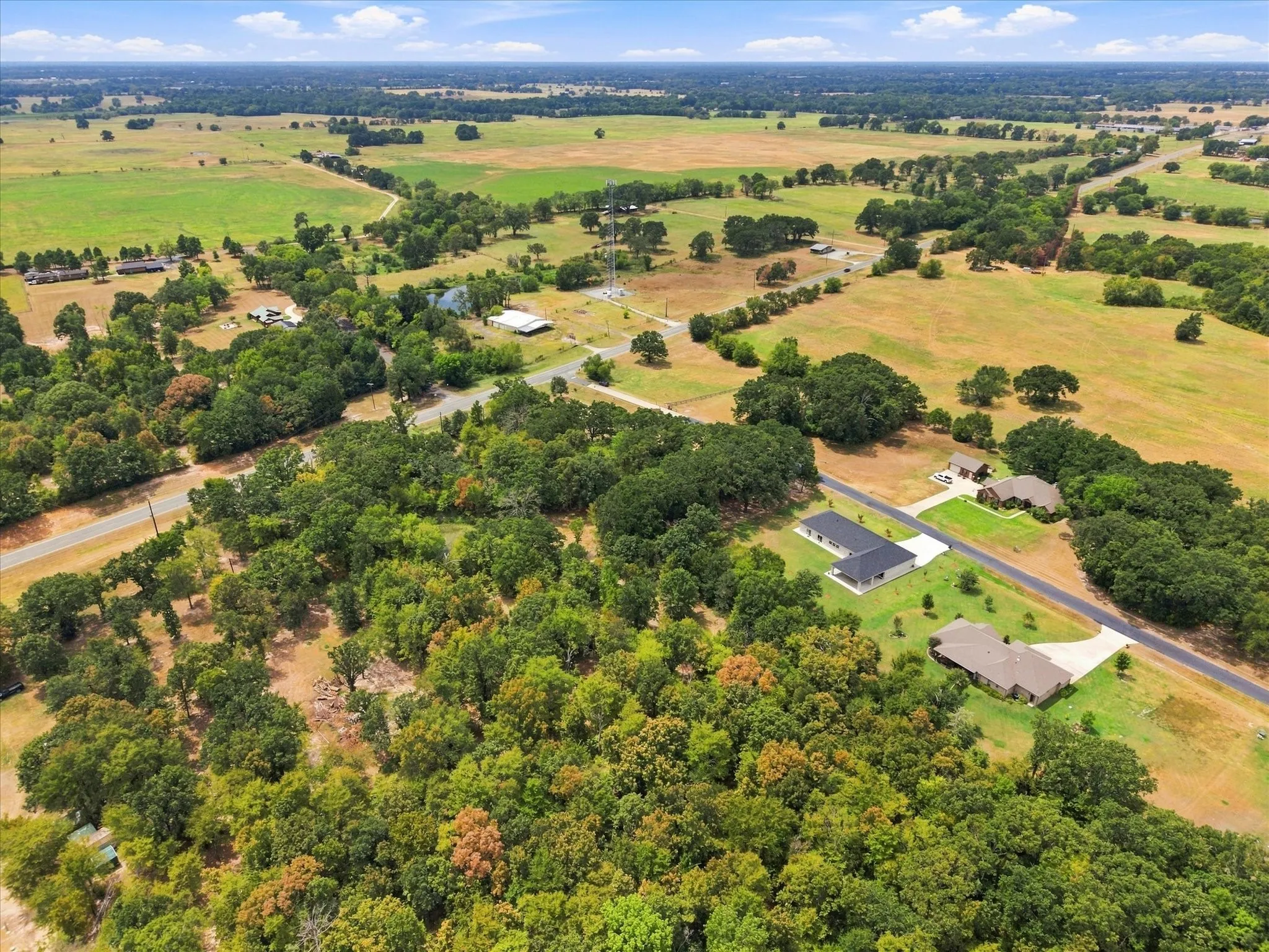 Expansive land featuring mature trees, open fields, and residential properties