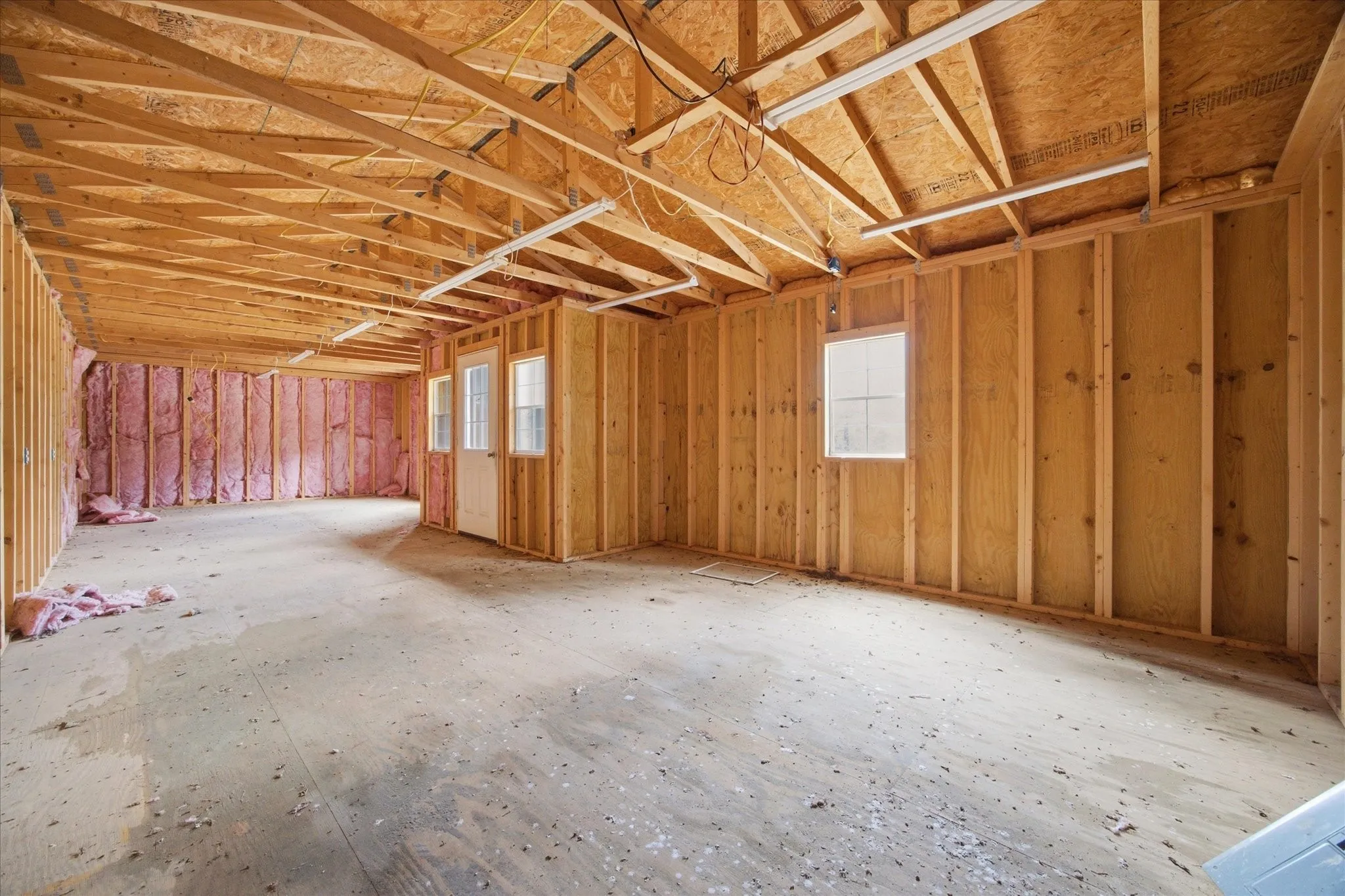 Unfinished interior space featuring exposed wood framing, ceiling trusses, an interior door with glass panels, and multiple windows