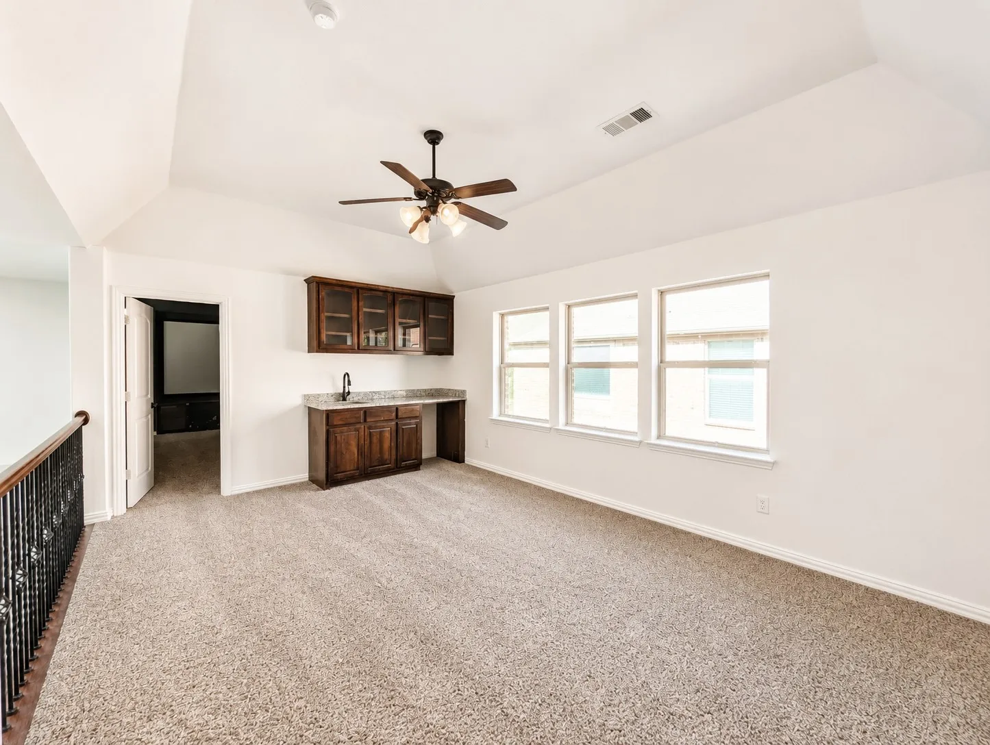 Vaulted ceiling with a ceiling fan, built-in cabinetry with a sink, three windows, and carpet flooring
