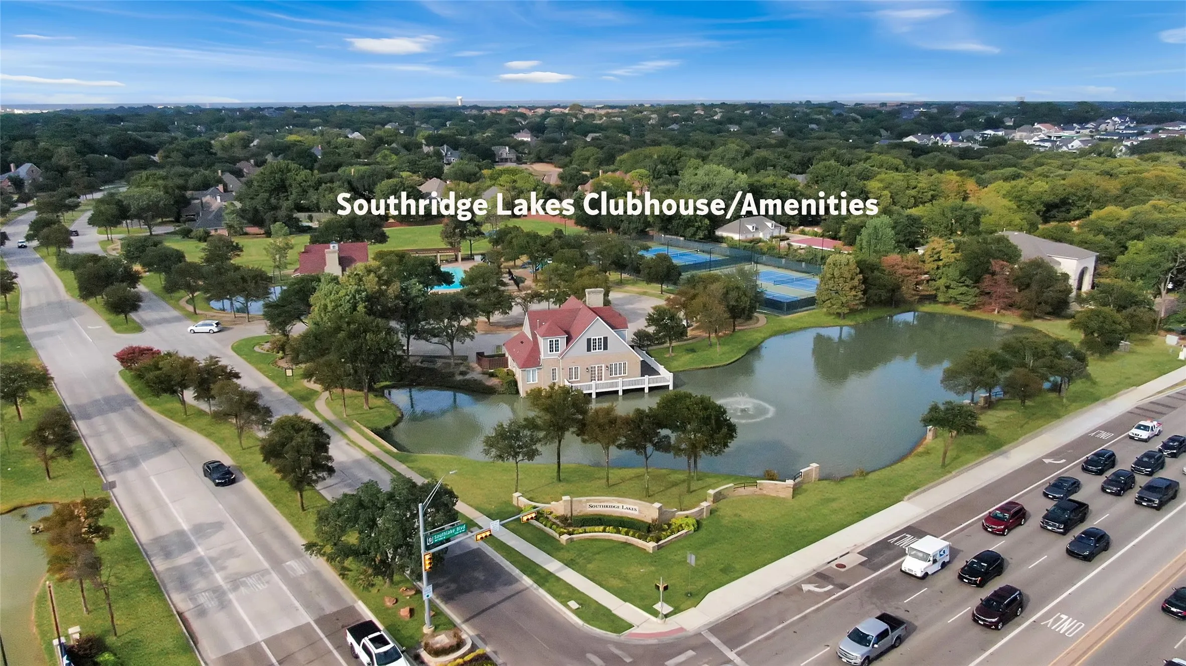 Drone view of entrance to subdivision with clubhouse, swimming pool and tennis courts