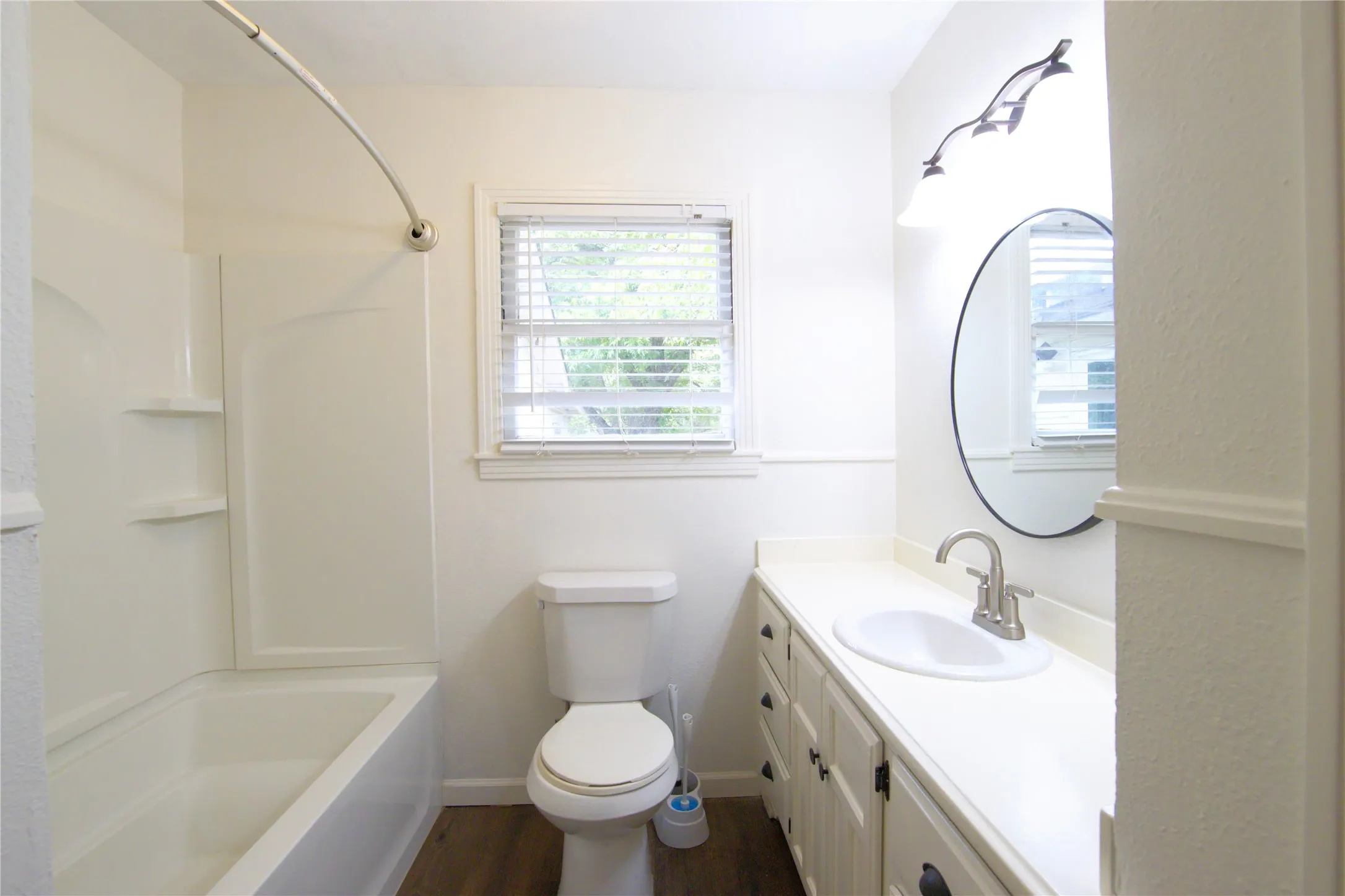 Bathroom featuring a single vanity with storage, a drop-in sink, a wall-mounted light fixture, and a tub/shower combination