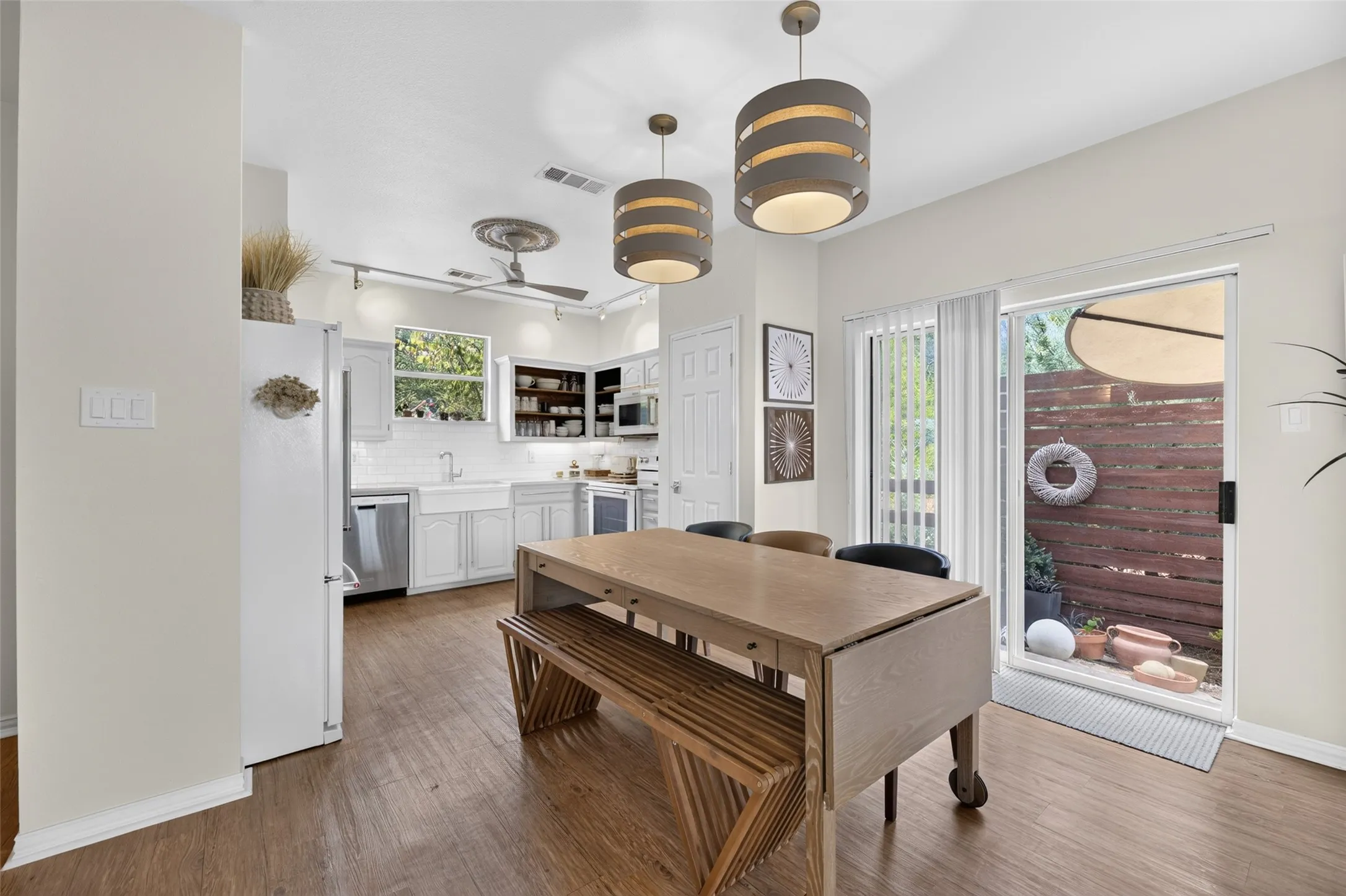 Kitchen with wood-finish flooring, white cabinetry, a farmhouse sink, stainless steel appliances, and two pendant light fixtures