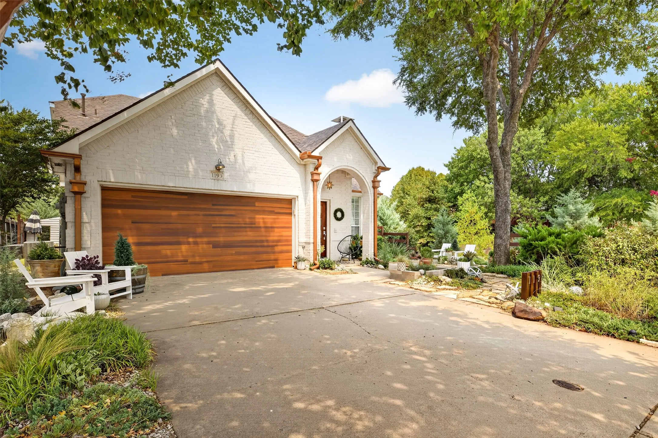 White brick exterior featuring a wood-finish garage door, arched entry, and copper-toned gutters