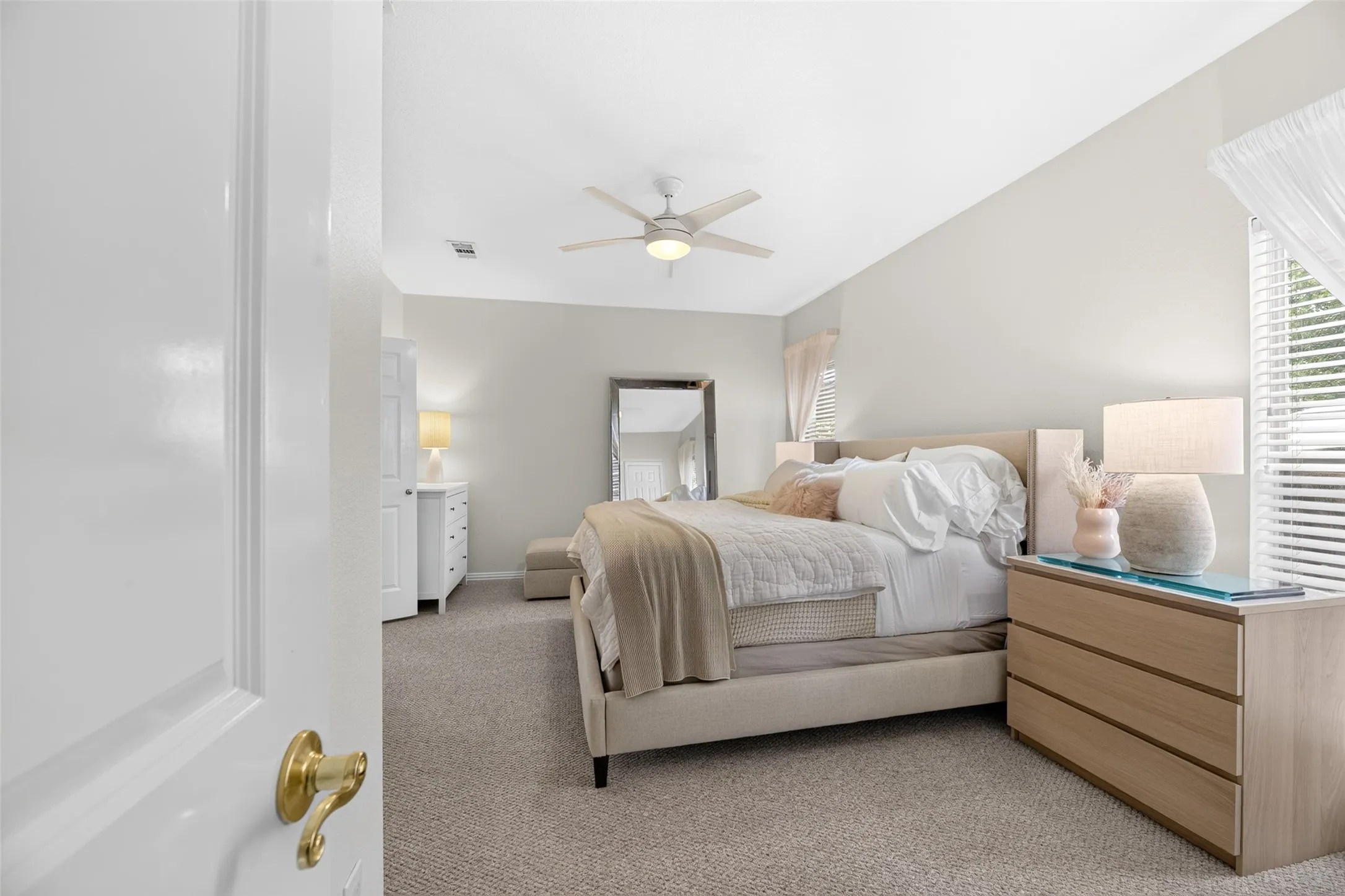 Vaulted ceiling, ceiling fan, white paneled door, brass door hardware, carpeted flooring