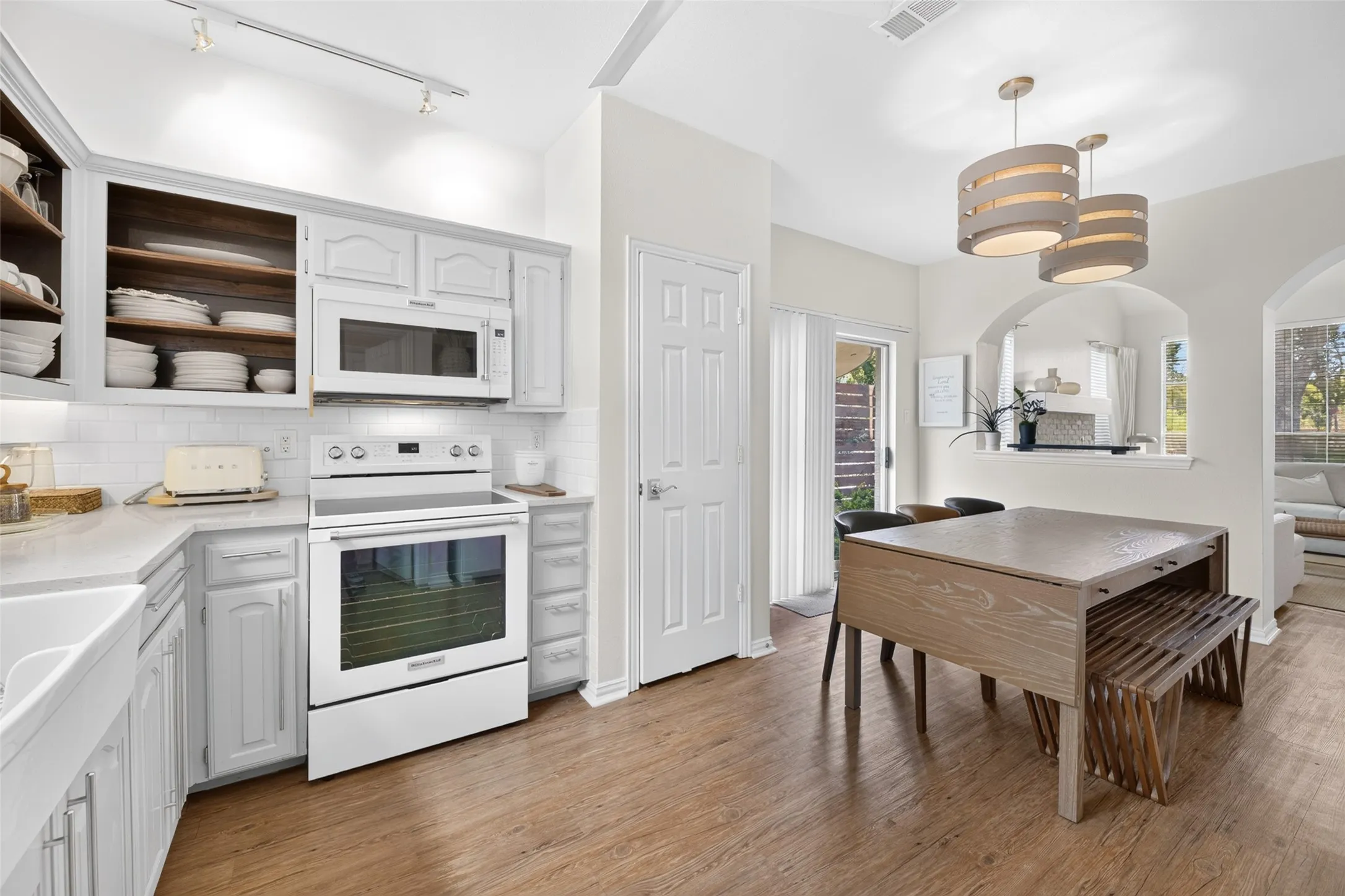 Contemporary kitchen featuring white cabinetry, subway tile backsplash, white appliances, track lighting, and wood-finish flooring